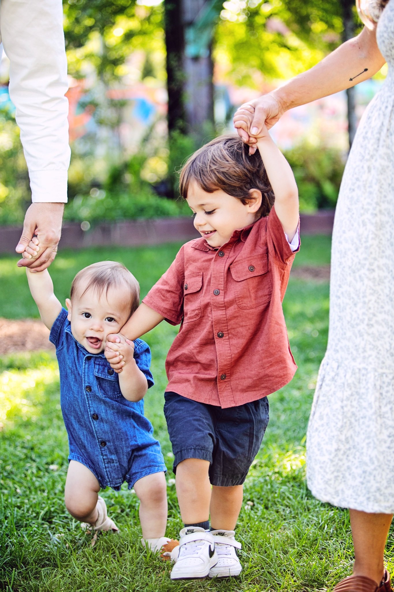 Two little brothers walking across the grass, each holding a parent’s hand