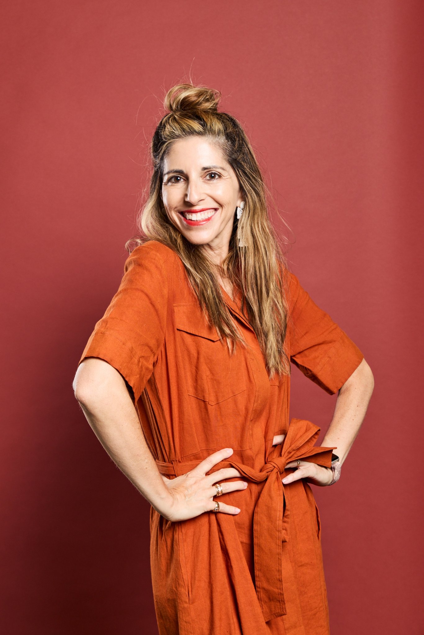 Jami, Daysee co-founder, smiling in a rust shirt dress on a red backdrop