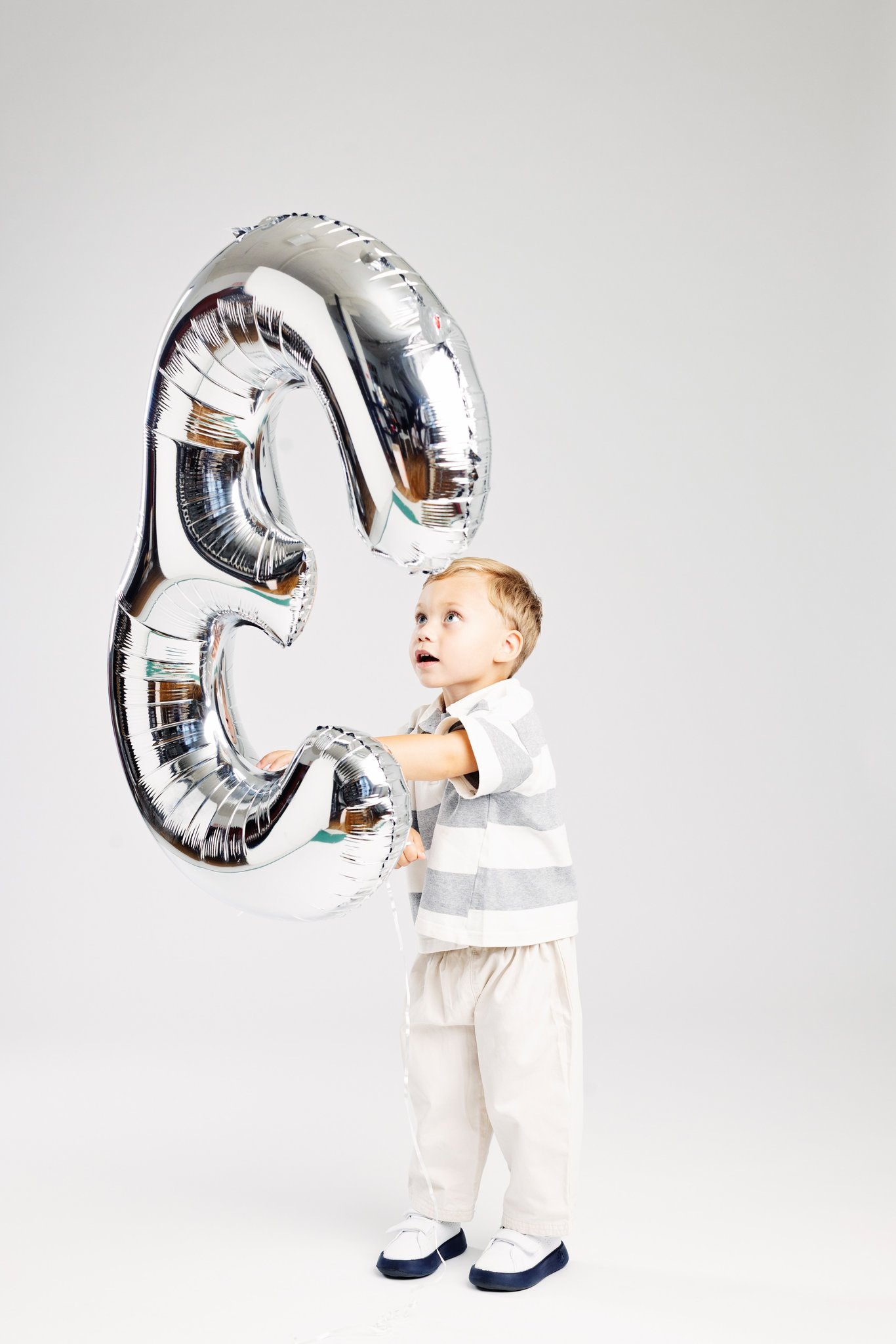 A boy looking up at a silver number-three balloon