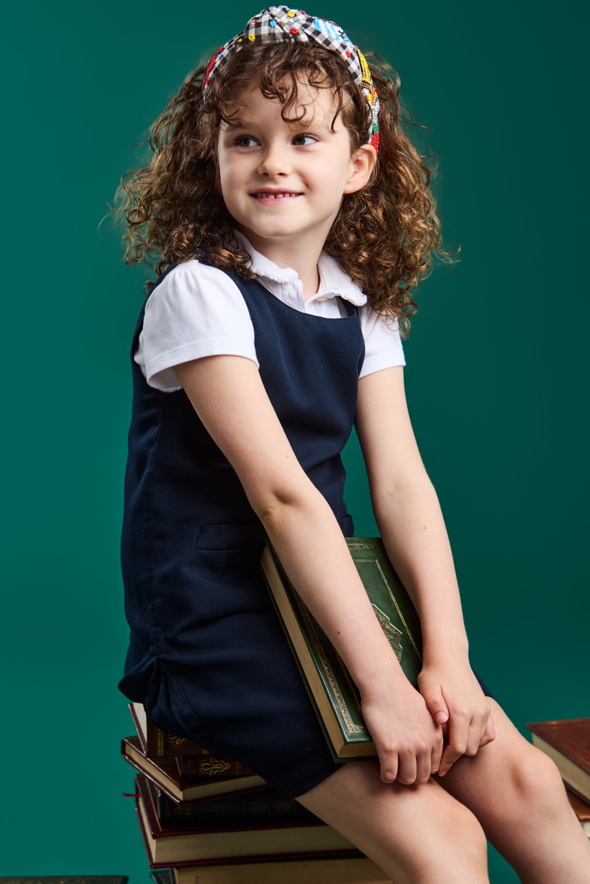 A girl in a navy uniform sitting on a stack of books