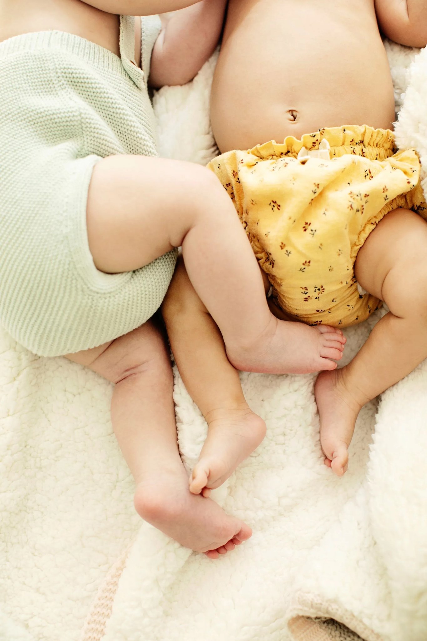 Two babies lying side by side on a soft blanket