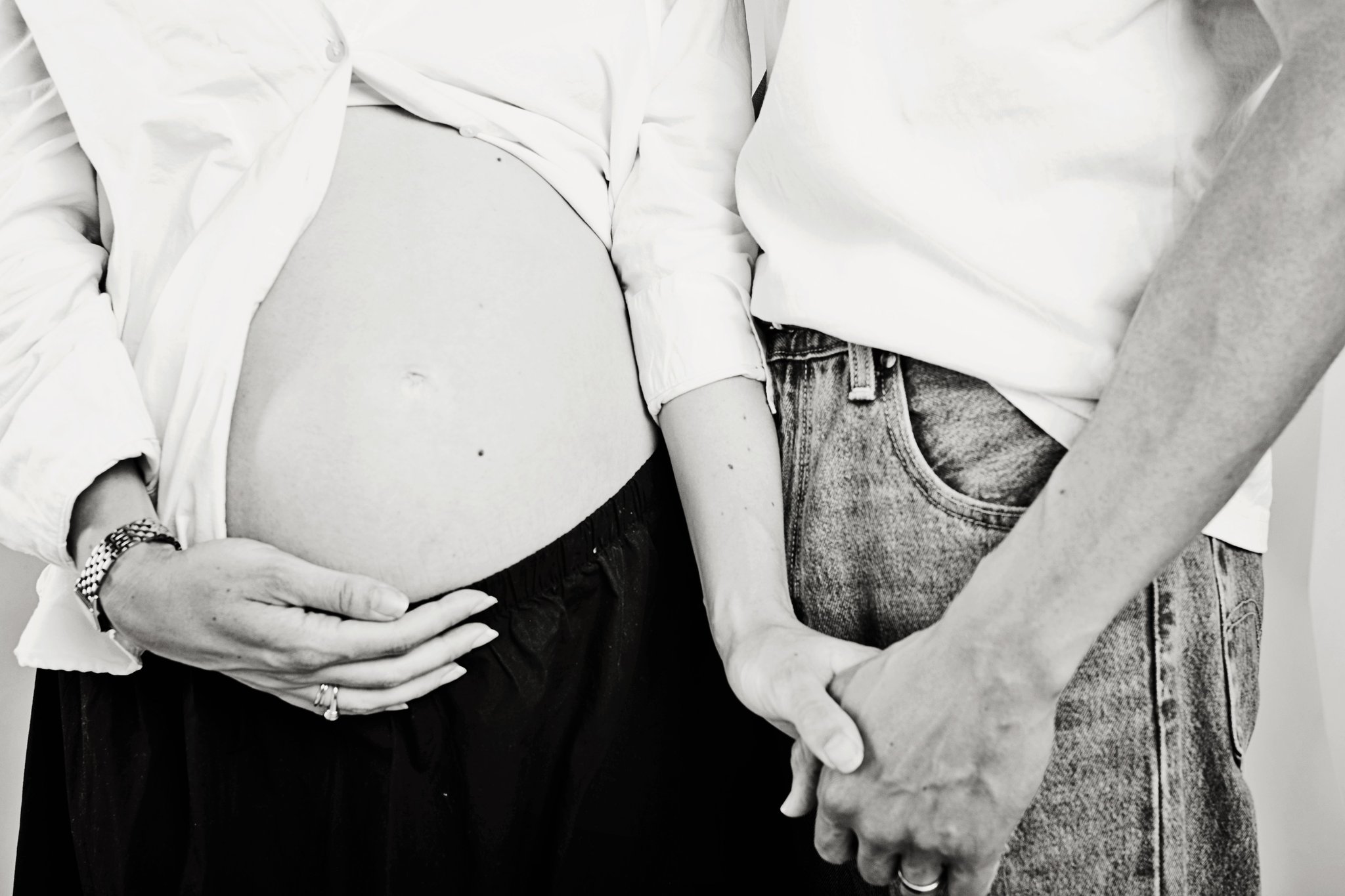 An expecting couple holding hands beside the bump, in black and white