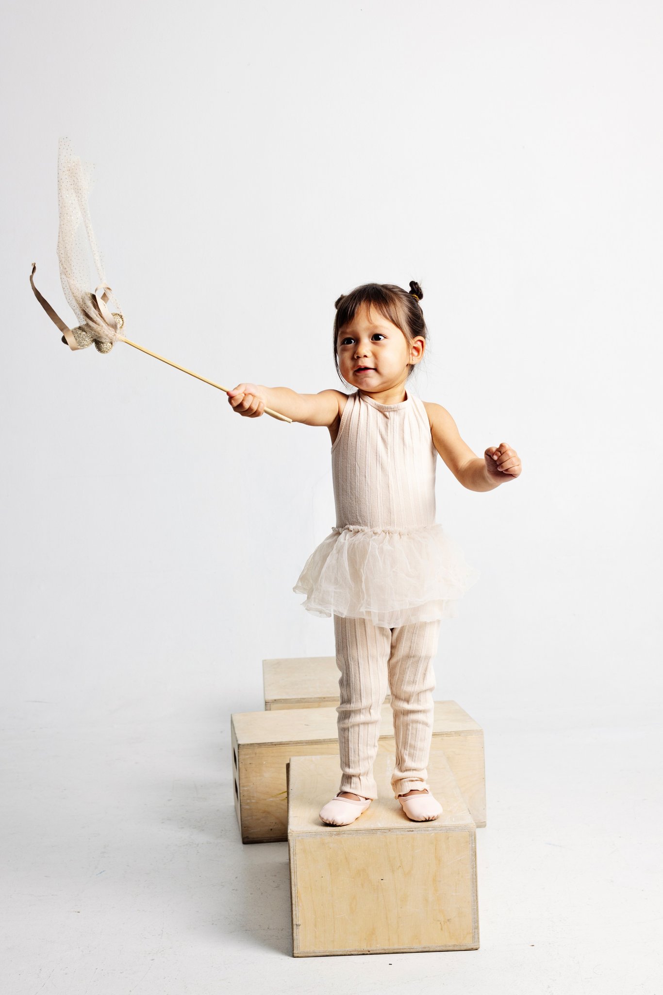 A girl in a tutu waving a wand on apple boxes