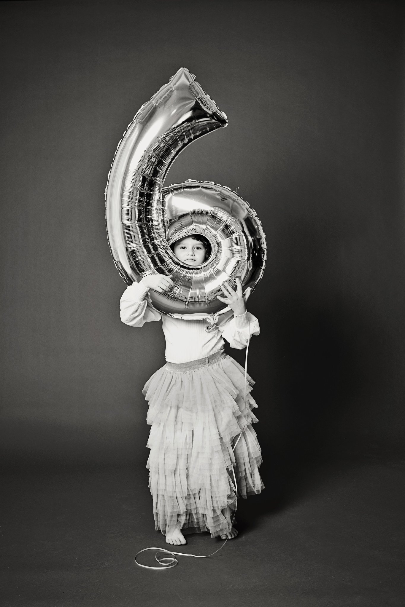 A girl framed by a silver six balloon in black and white