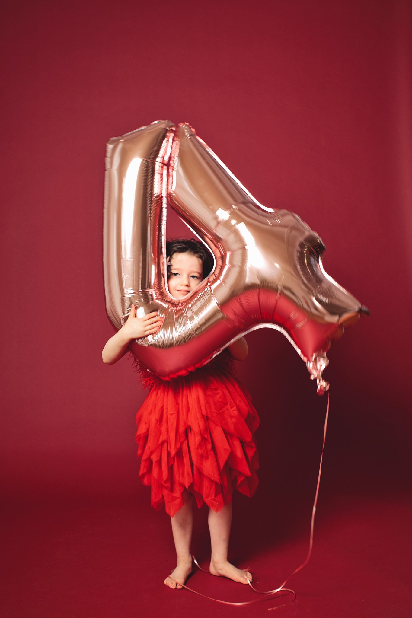 A girl in red with her head through a number-four balloon