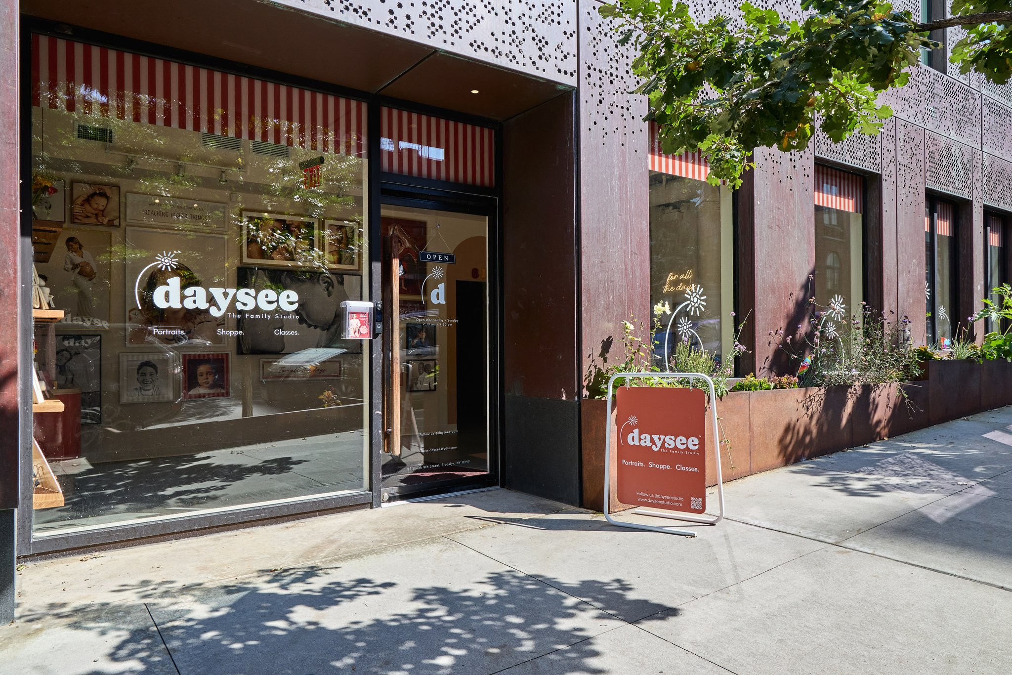 The daysee storefront on South 4th Street, with the logo and family portraits in the windows and a daysee sign on the sidewalk