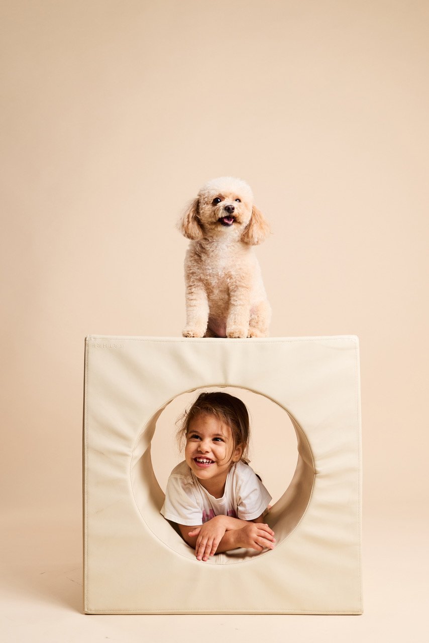 A toy poodle perched on top of a cube while a child peeks out through its round window