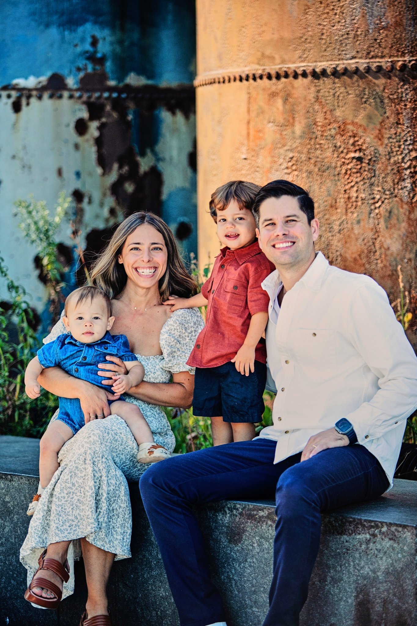 A smiling family of four sitting together beside rusted steel tanks