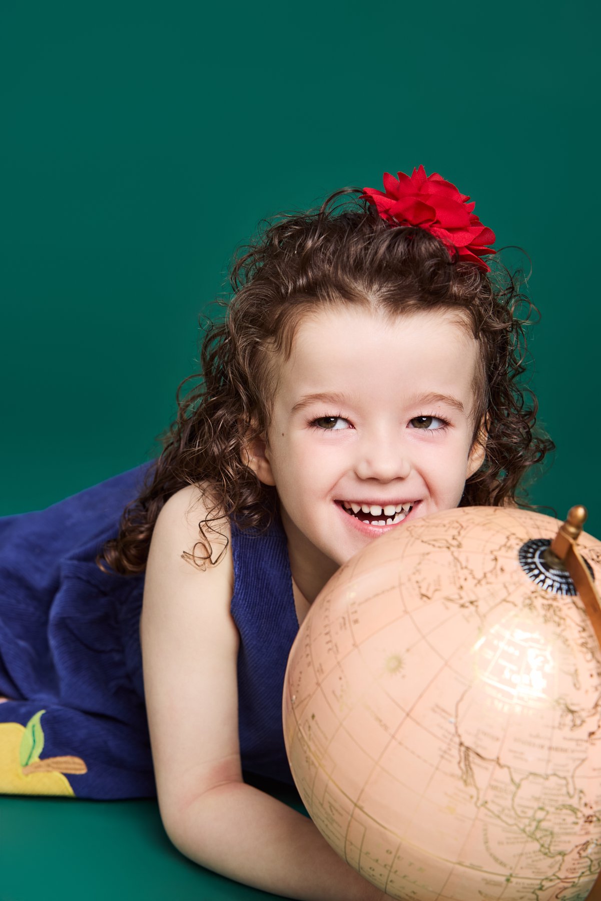 A girl lying beside a globe, grinning