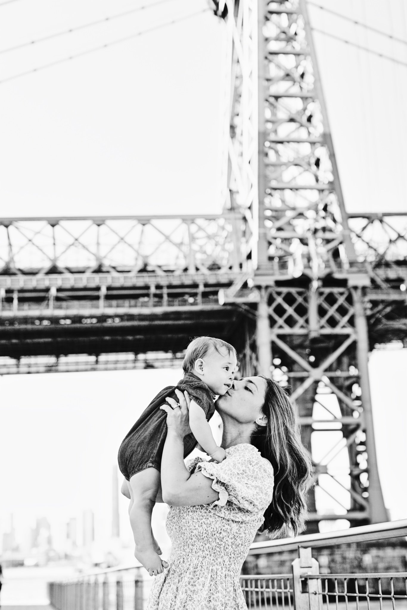 A mother kissing her baby beneath the Williamsburg Bridge, in black and white