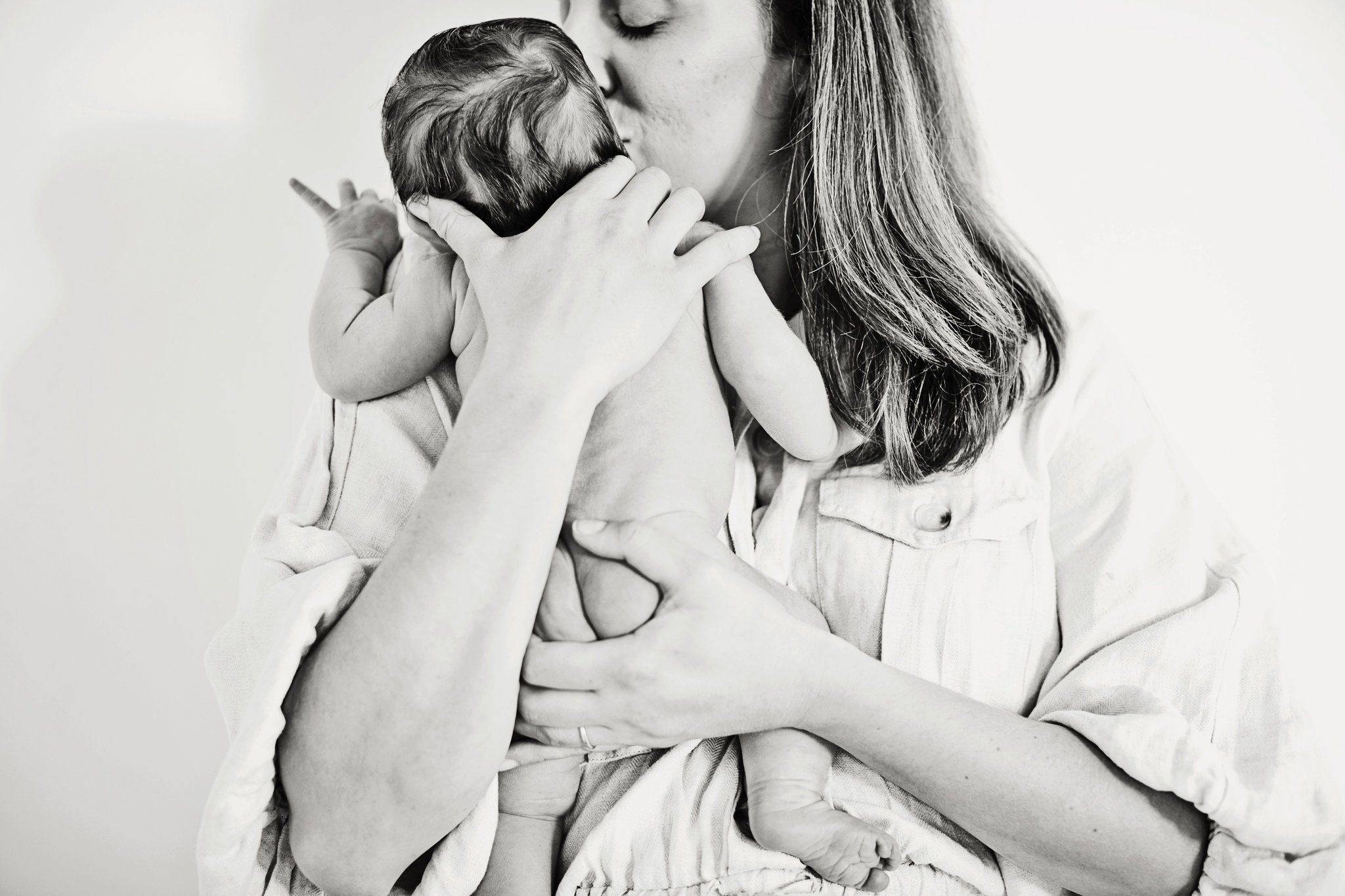 A mother kissing her newborn’s head, in black and white