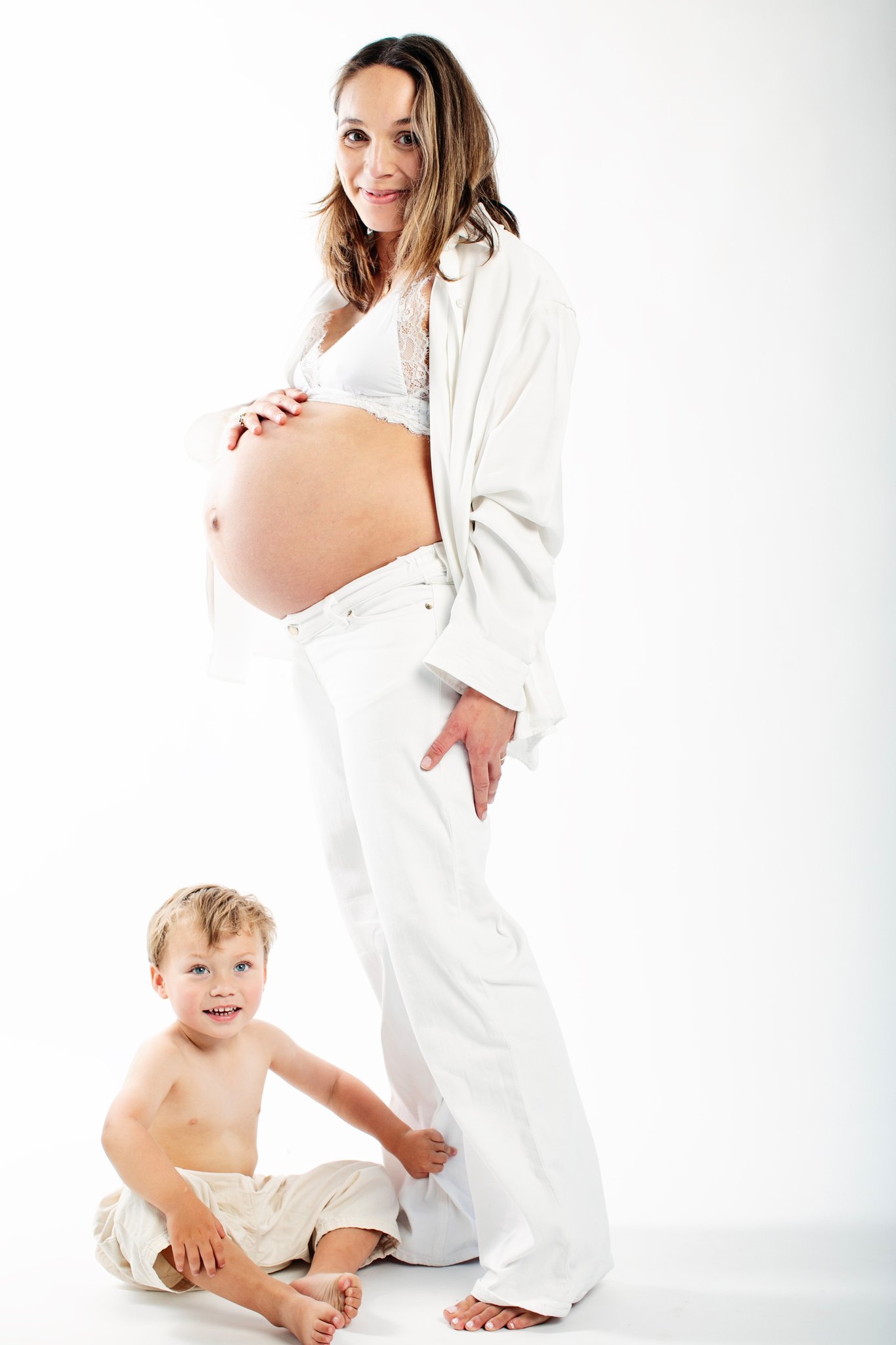 An expecting mother in cream standing with her son