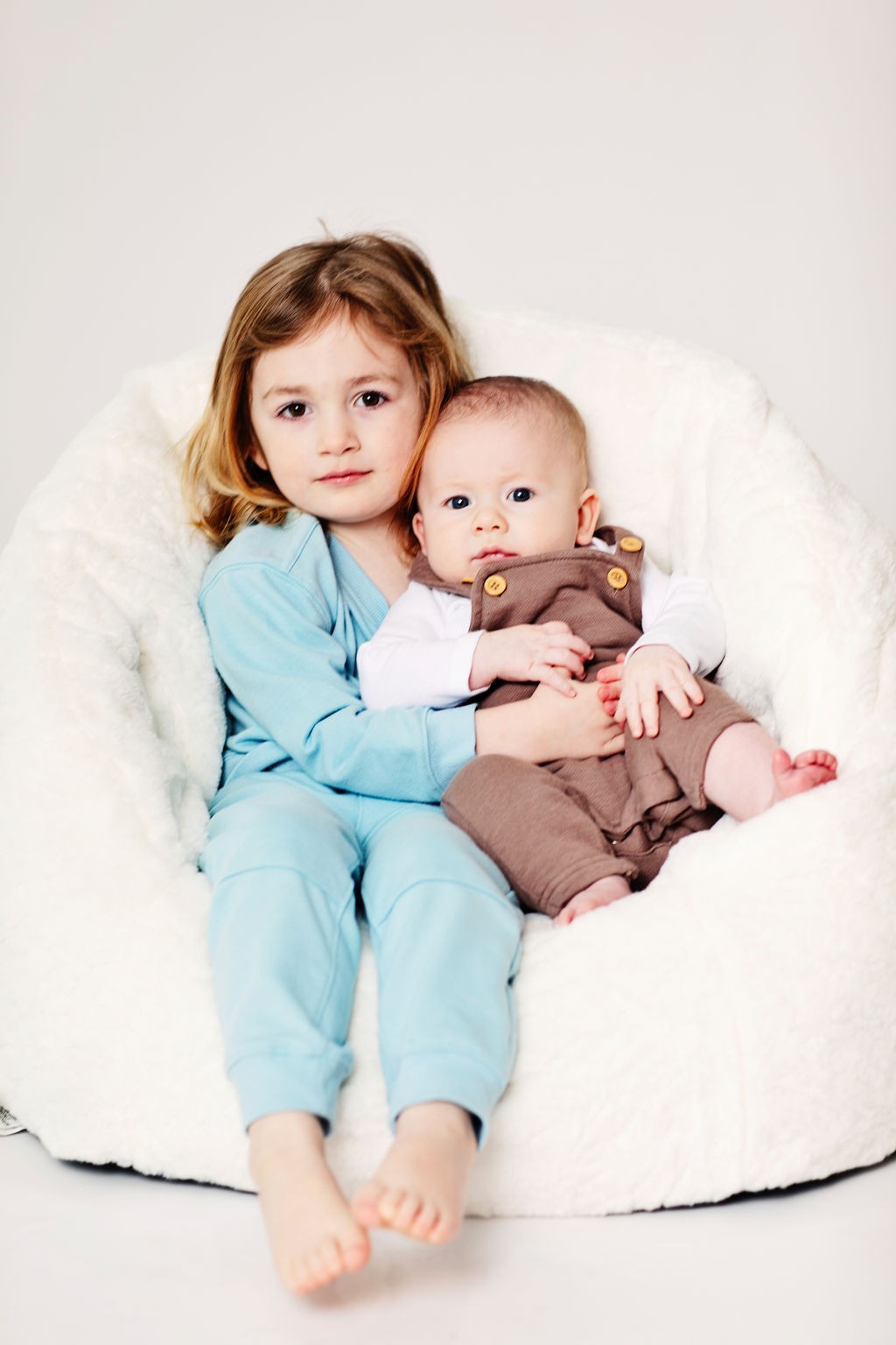 A big sister holding her baby brother in a white beanbag chair
