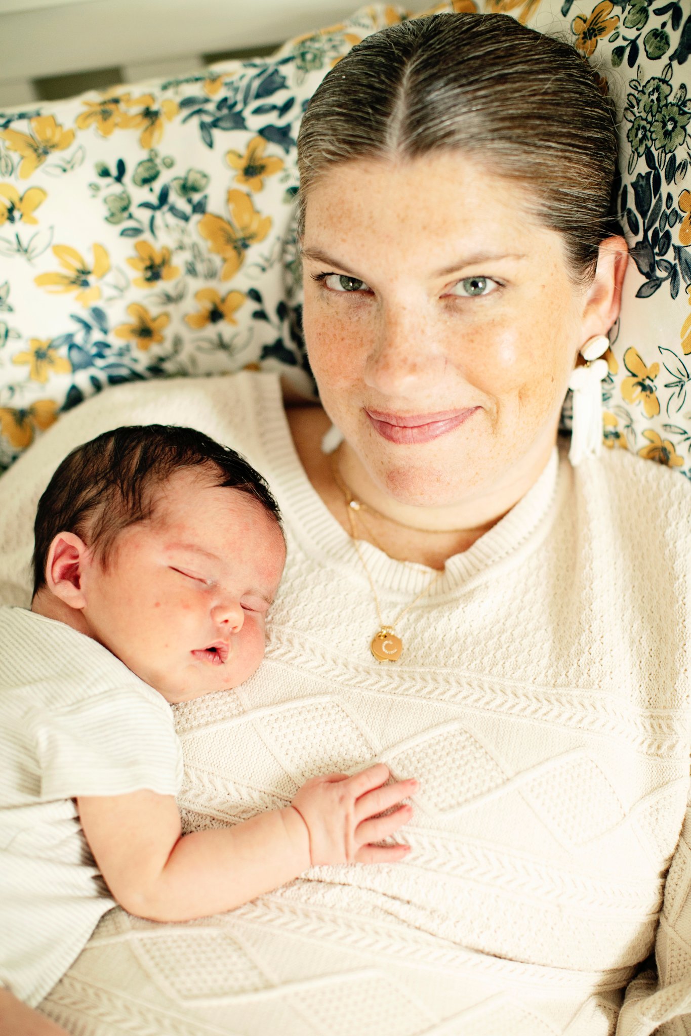 A mother holding her sleeping newborn in a floral armchair