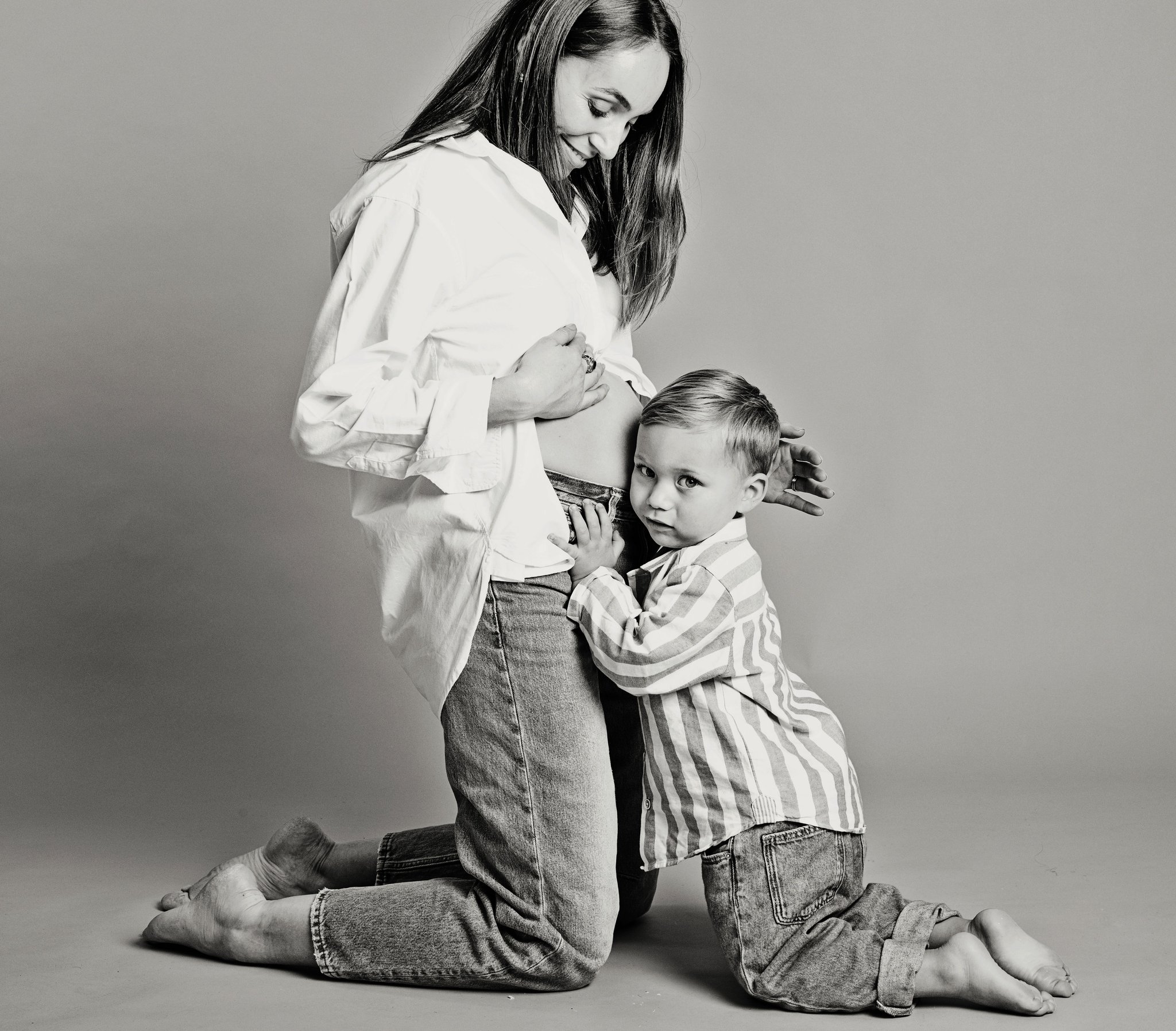 A boy leaning on his mother’s bump, in black and white
