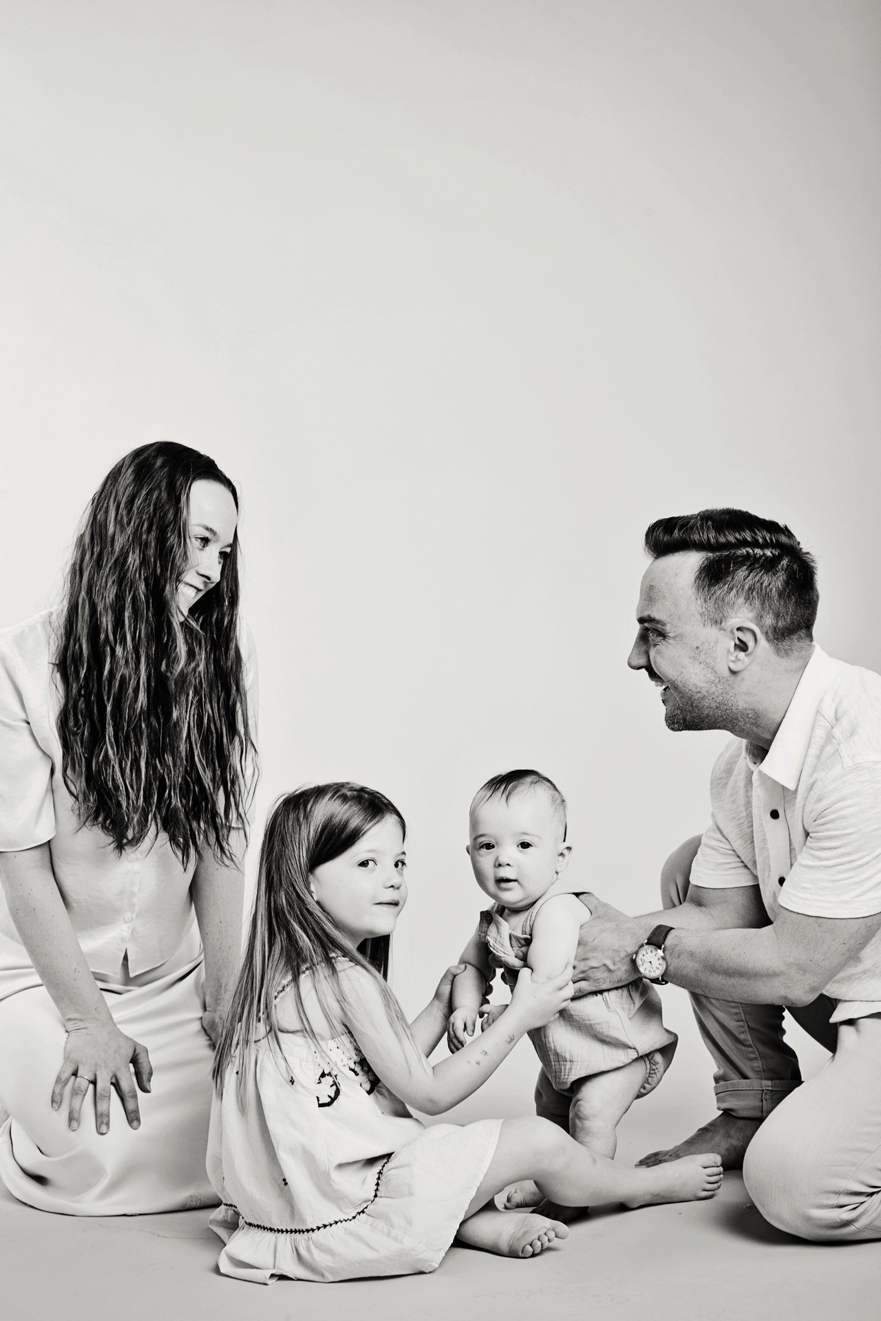A family of four sitting together on a light backdrop, in black and white