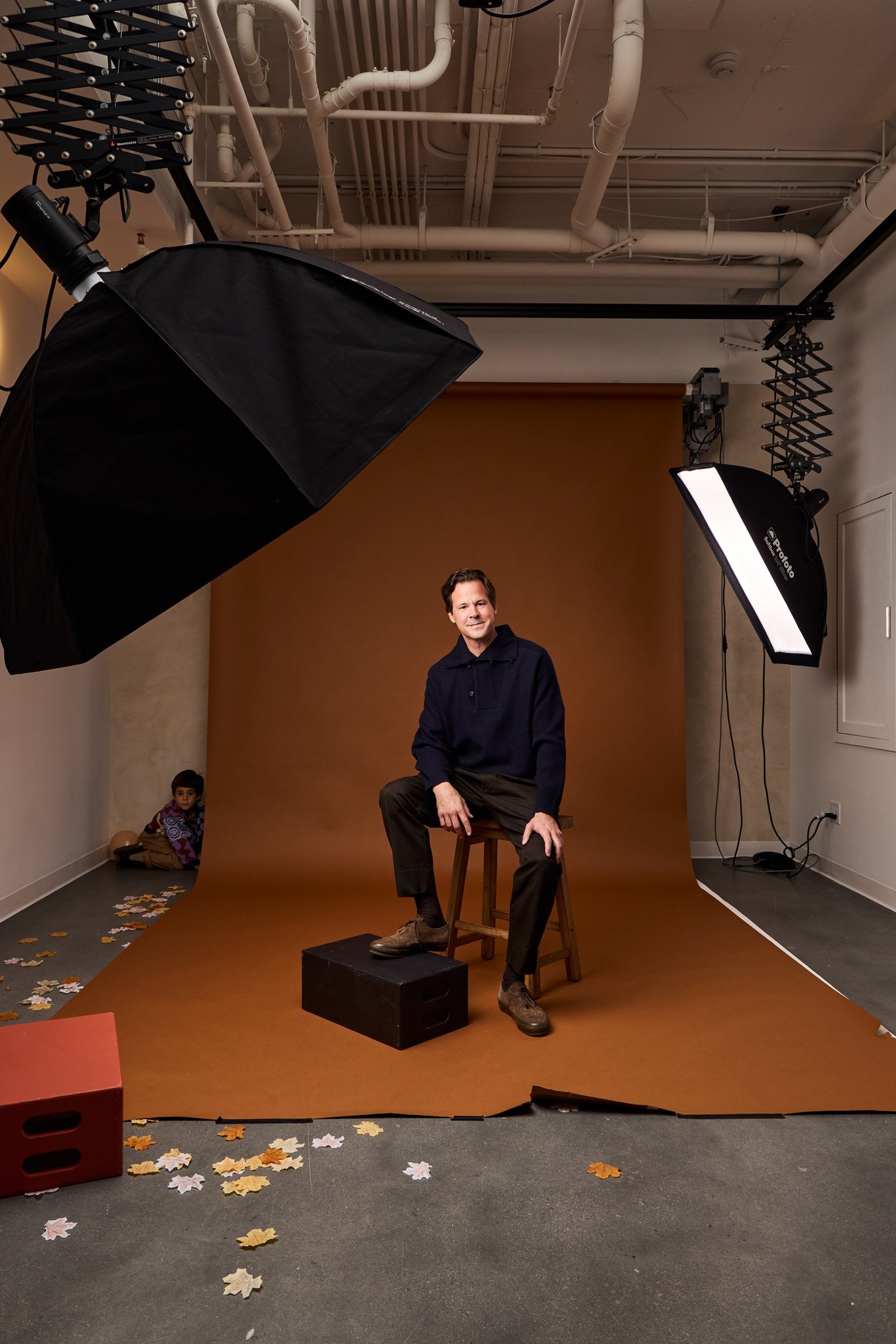 The Daysee studio set for a shoot: a man on a stool against a rust paper backdrop between a softbox and a strip light