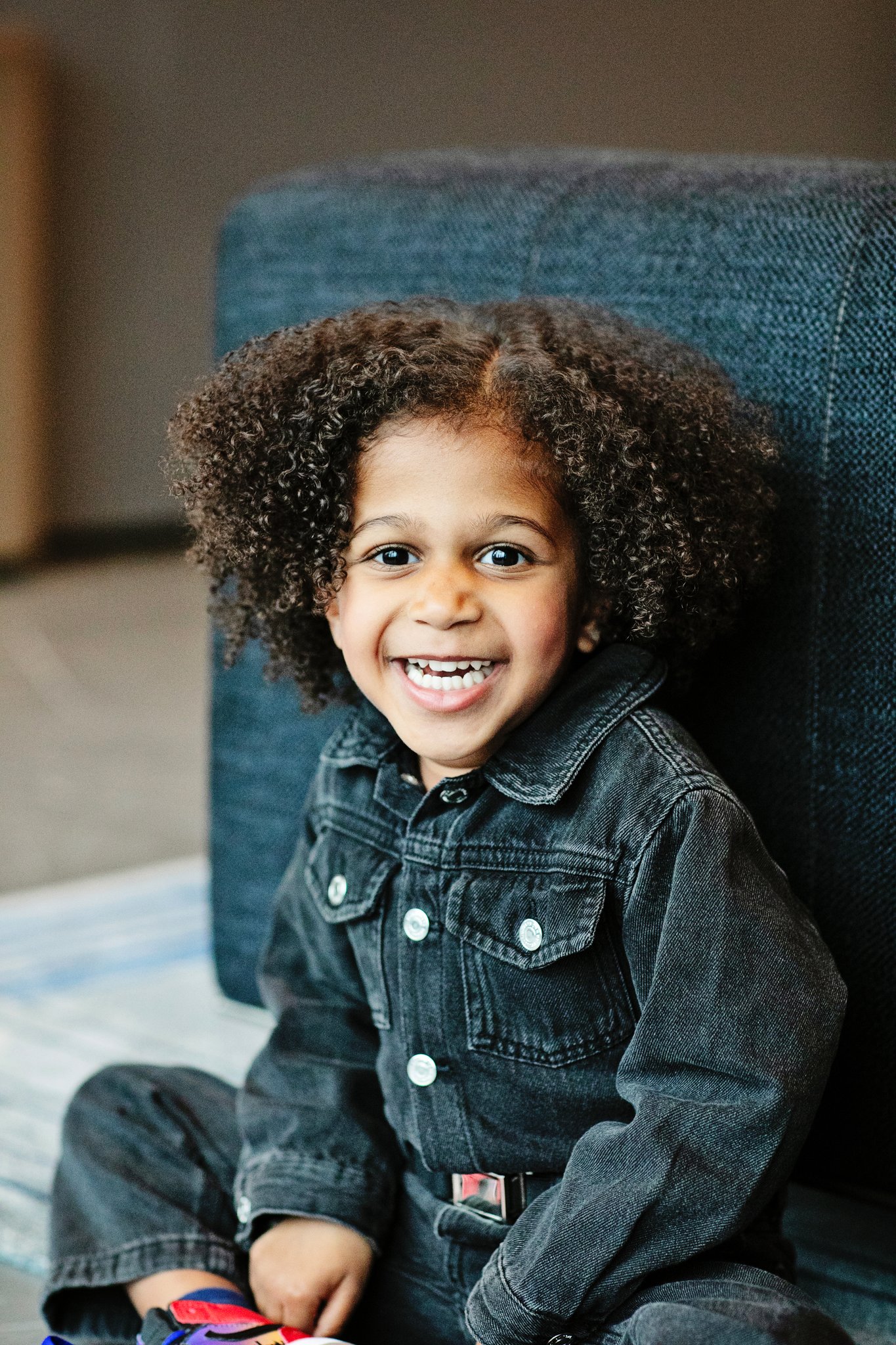A boy in a denim jacket laughing on the living room floor