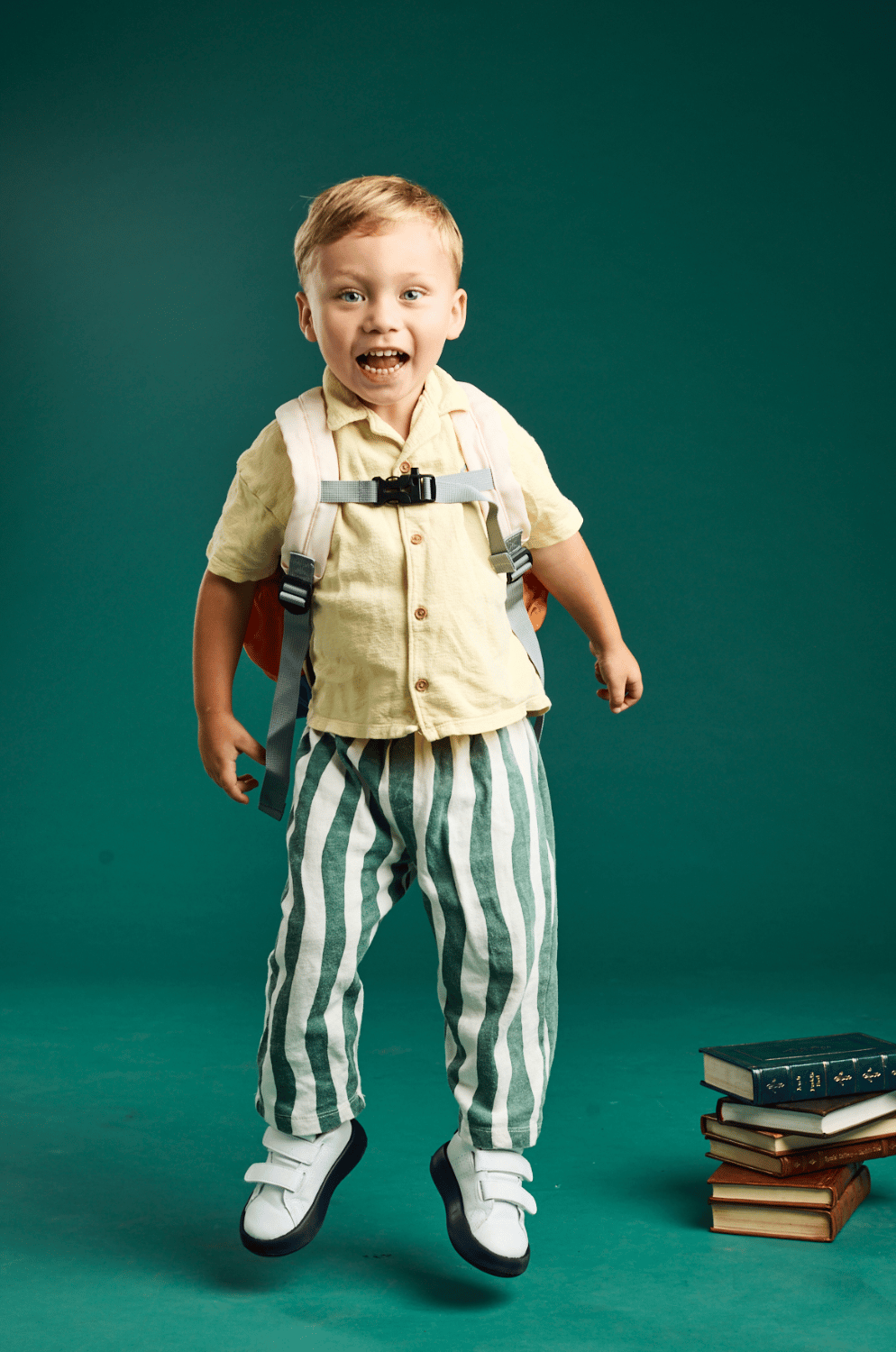 A boy jumping in striped pants with his backpack on