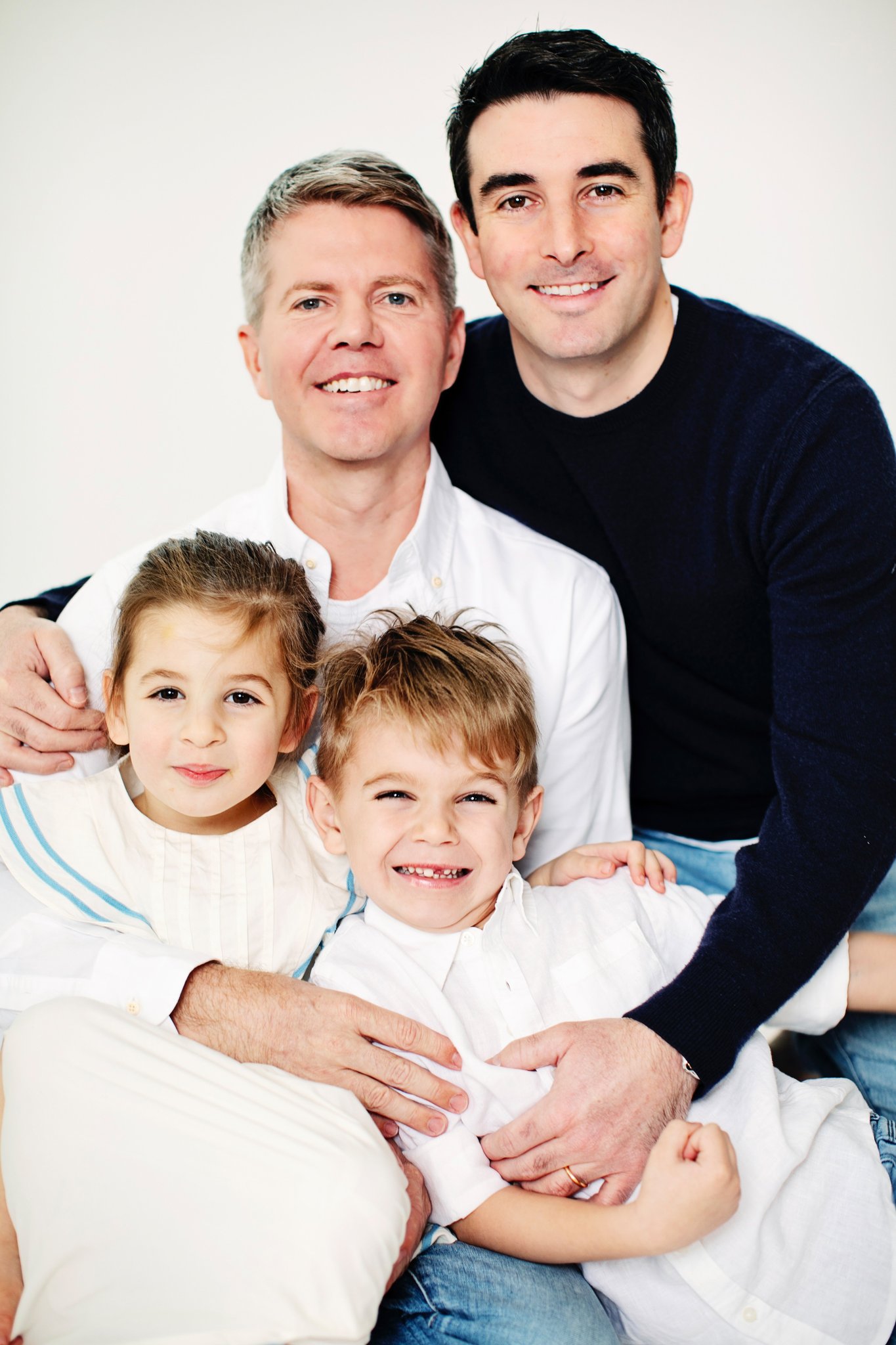 Two dads holding their children close