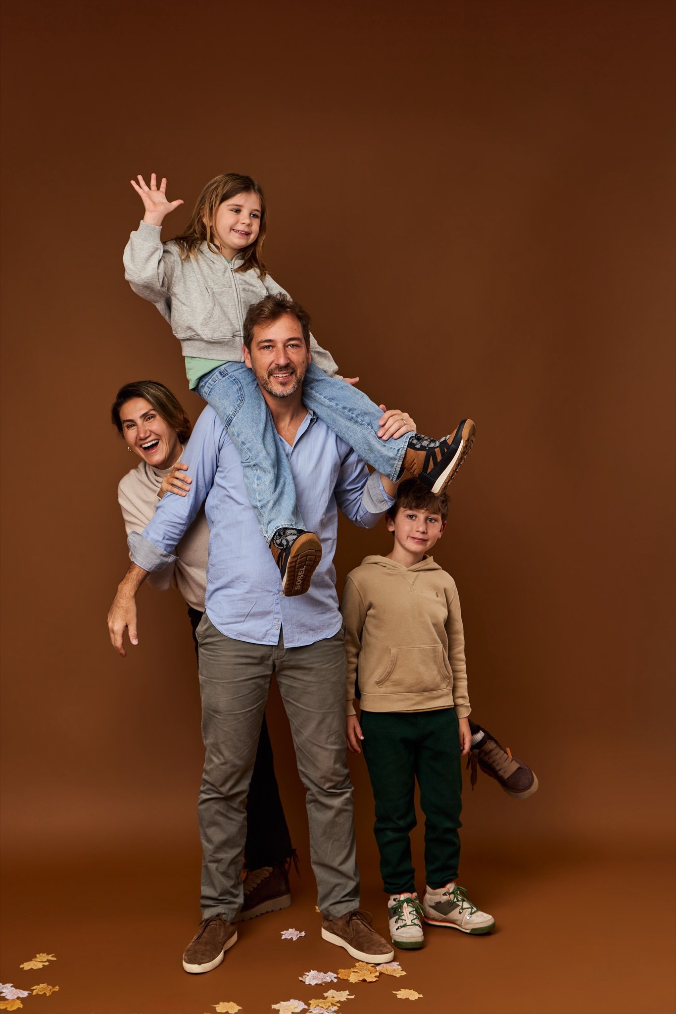 A girl waving from her father’s shoulders, with her mother peeking out behind them and her brother at their side, on the Cinnamon backdrop