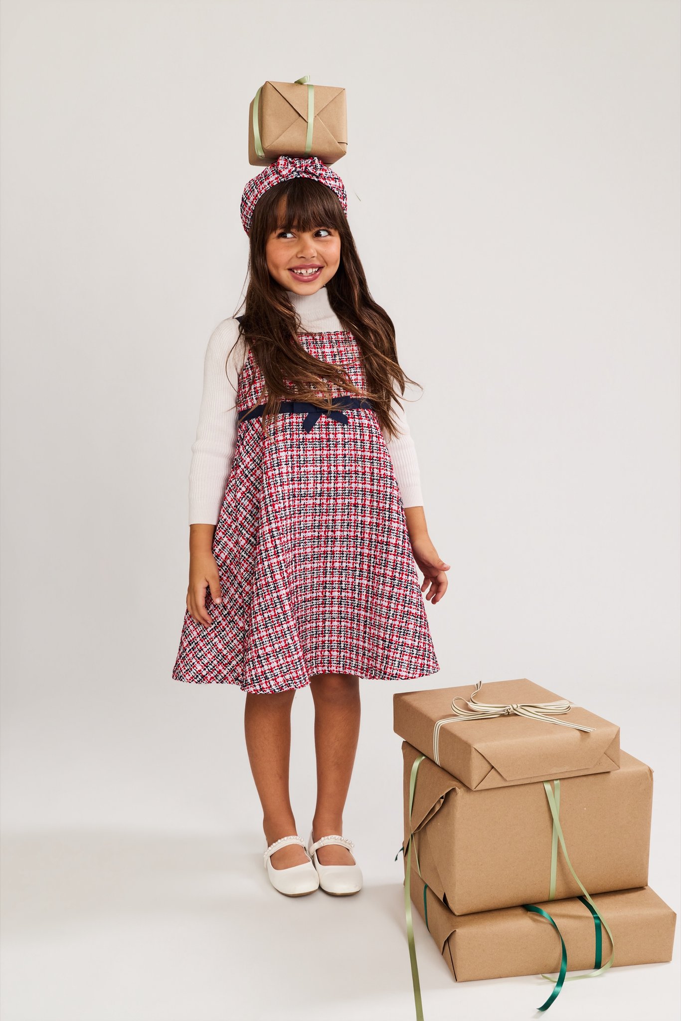 A girl balancing a wrapped gift on her head beside a stack of presents