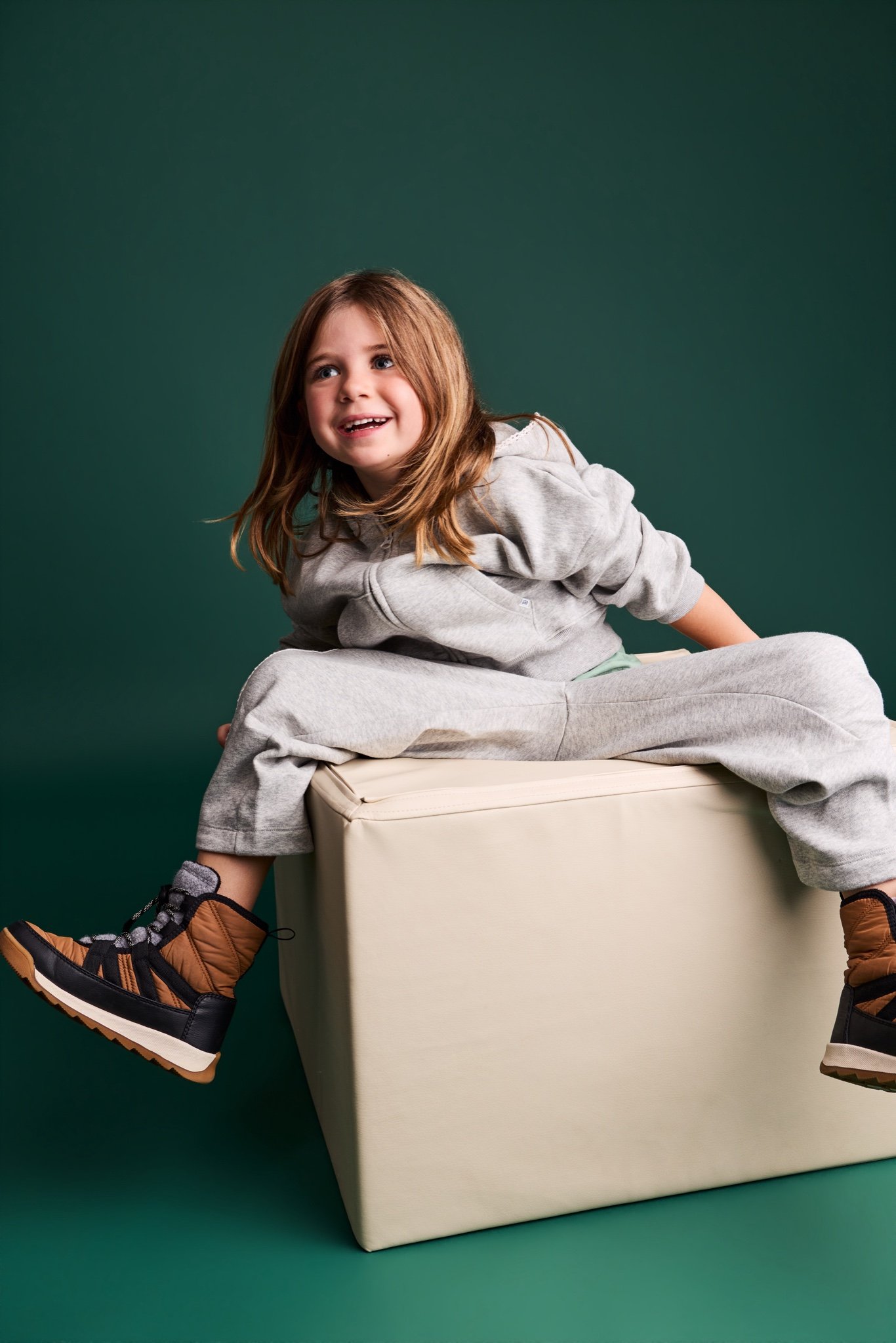 A girl in a grey tracksuit sitting on a cream block against the Evergreen backdrop