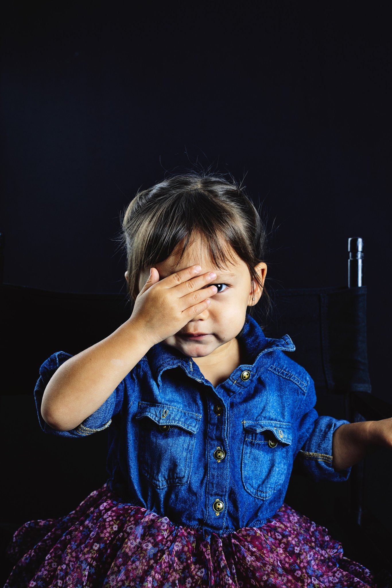 A girl in a denim shirt peeking through her hand