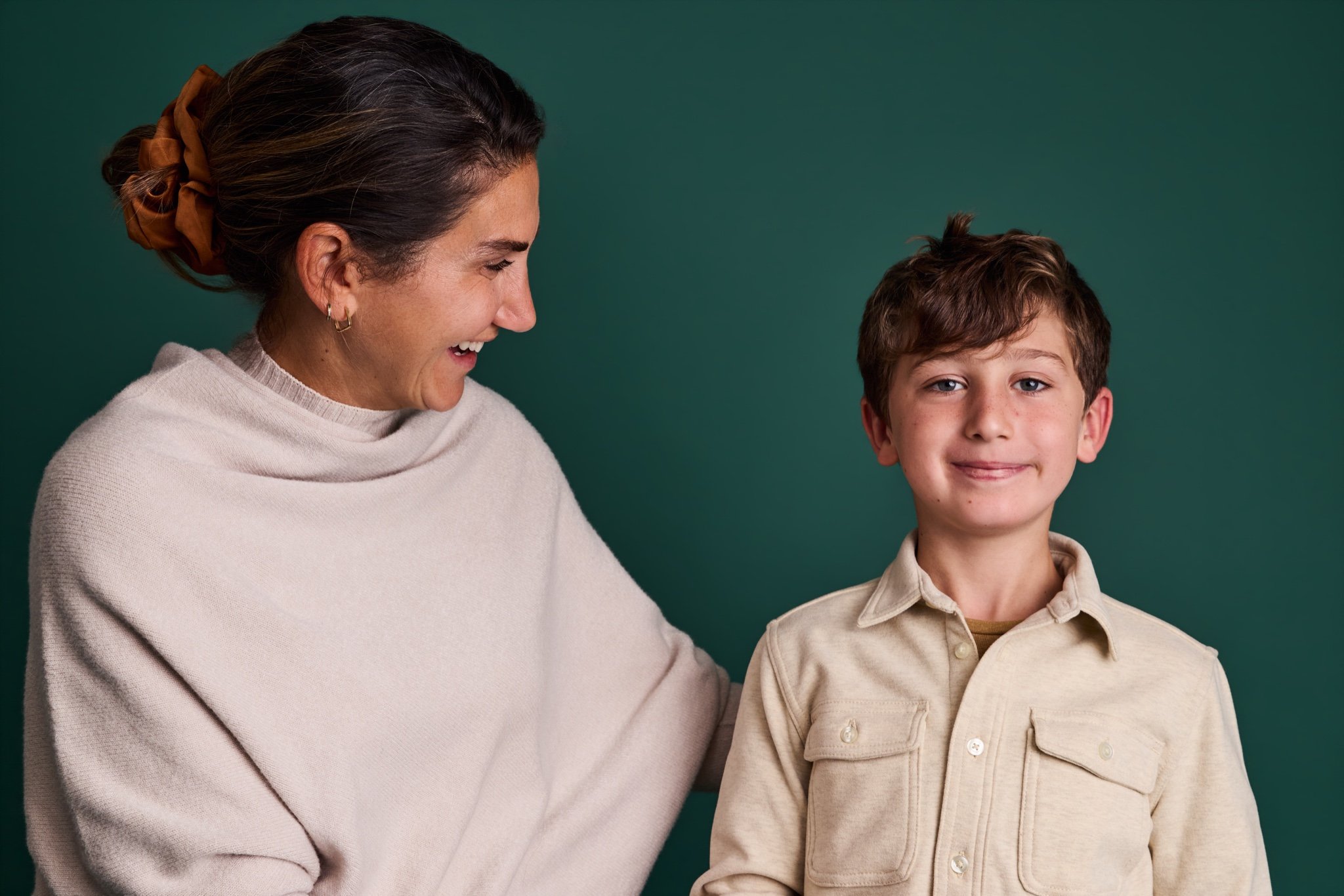 A mother in a cream wrap smiling down at her son on the Evergreen backdrop