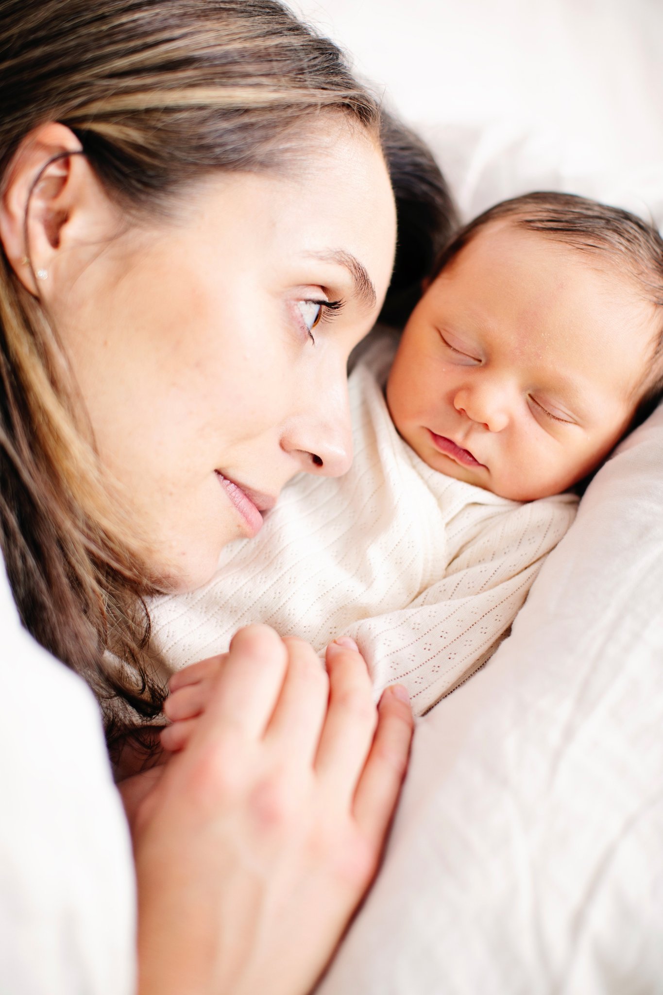 A mother resting cheek to cheek with her sleeping newborn