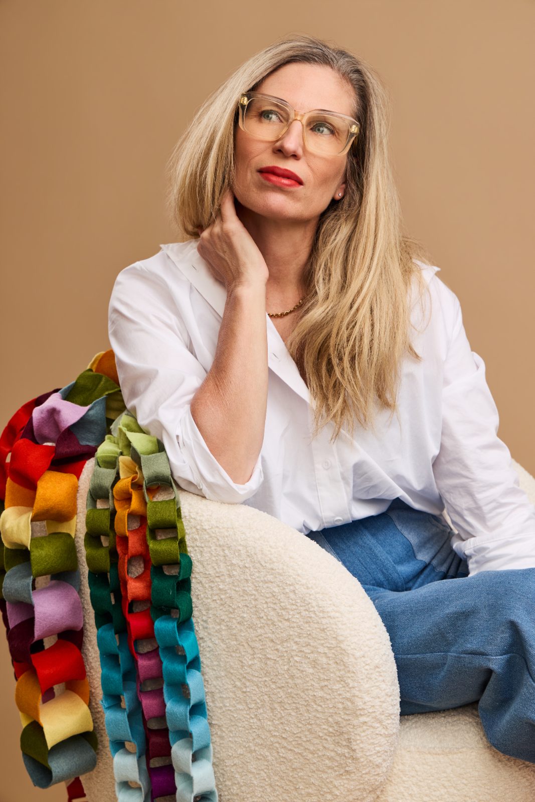 Portrait of a woman in clear glasses and a white shirt on a tan backdrop
