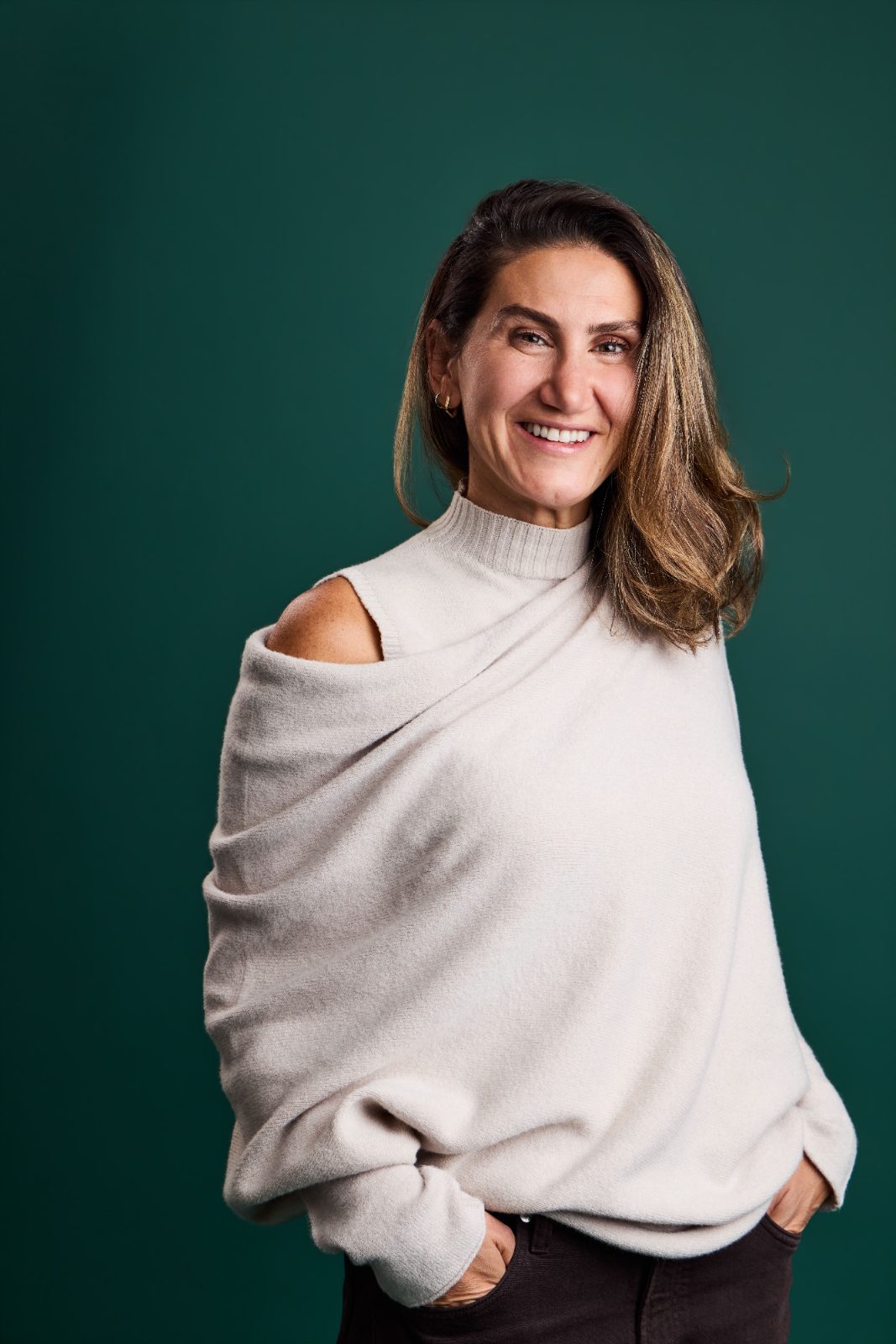 Portrait of a smiling woman in a draped cream sweater on a deep green backdrop