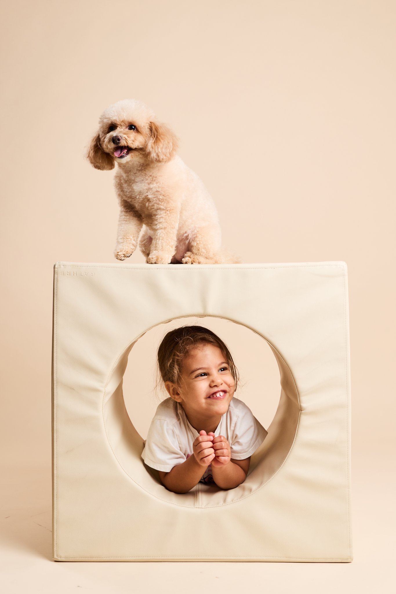 A toy poodle perched on top of a cube while a child peeks out through its round window