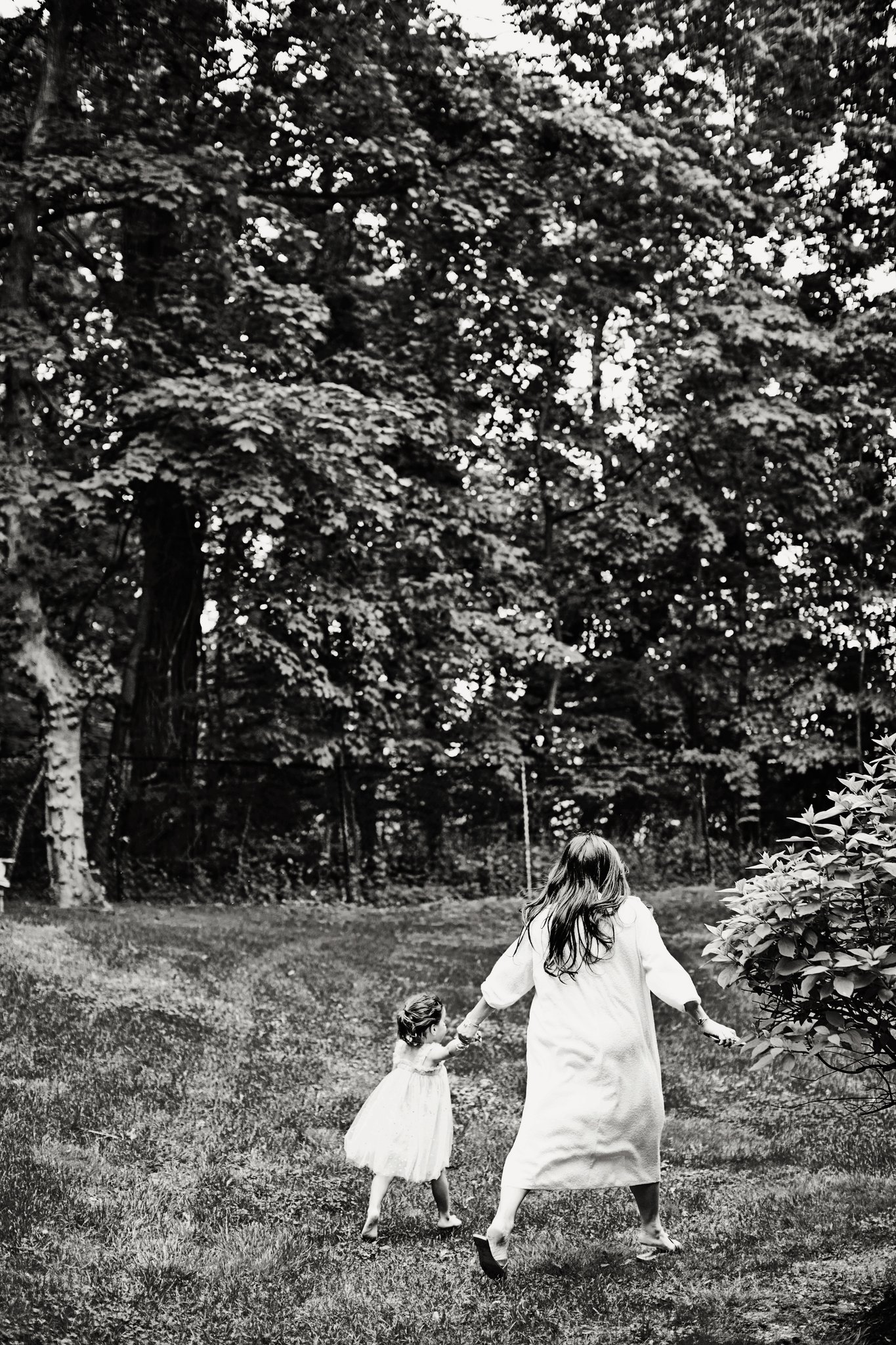 A mother and her daughter walking hand in hand across the grass, in black and white