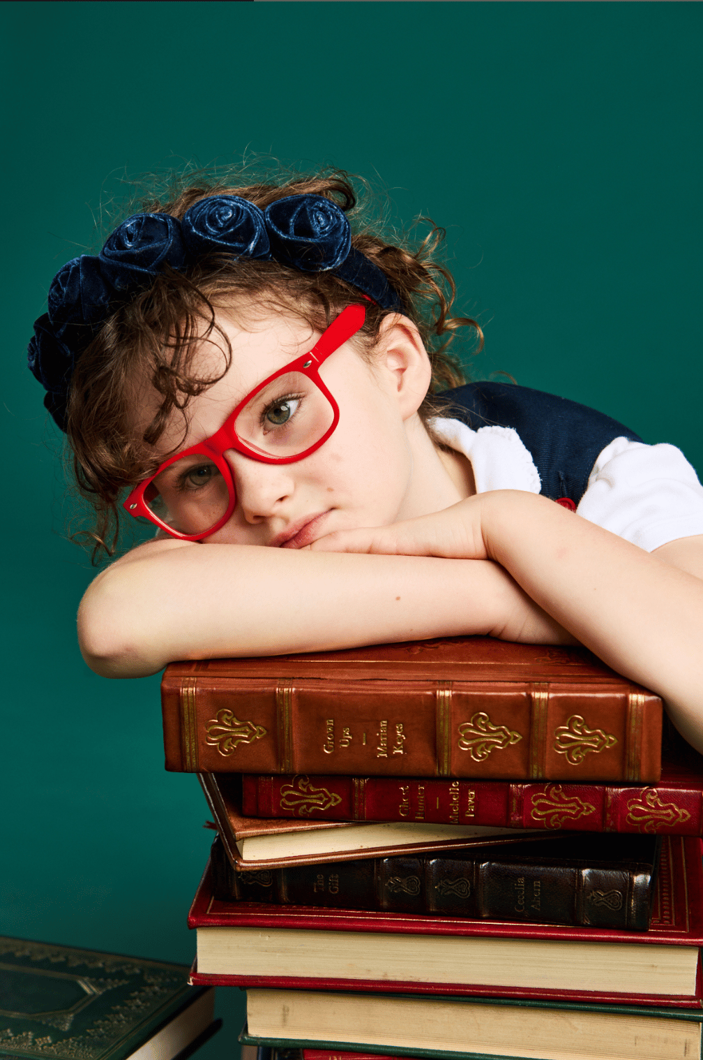 A girl in red glasses resting on a stack of books