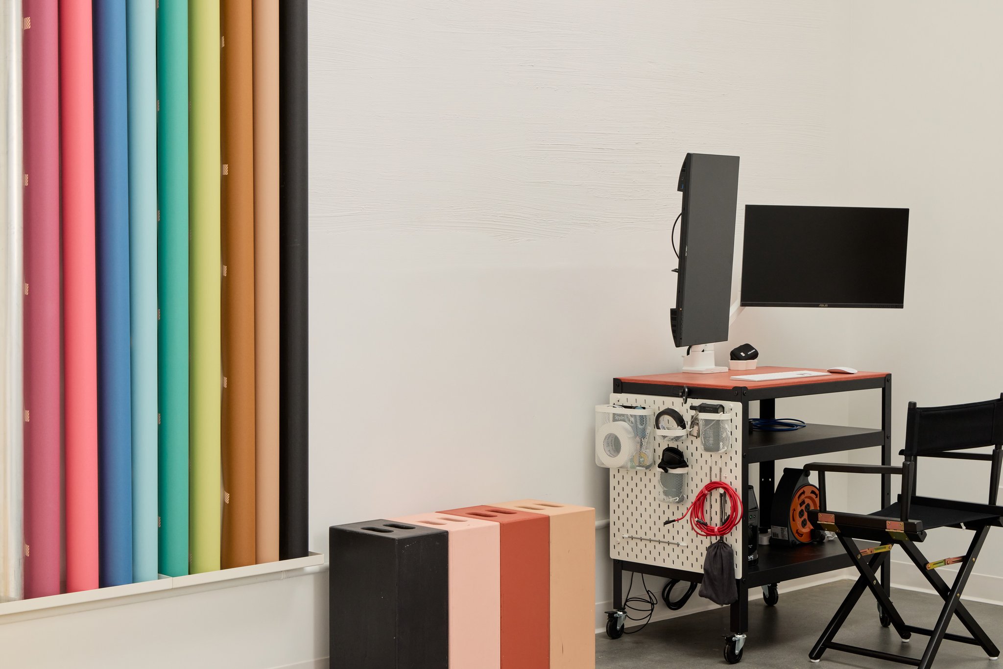 A wall of colored backdrop rolls beside black, pink, rust and peach posing blocks