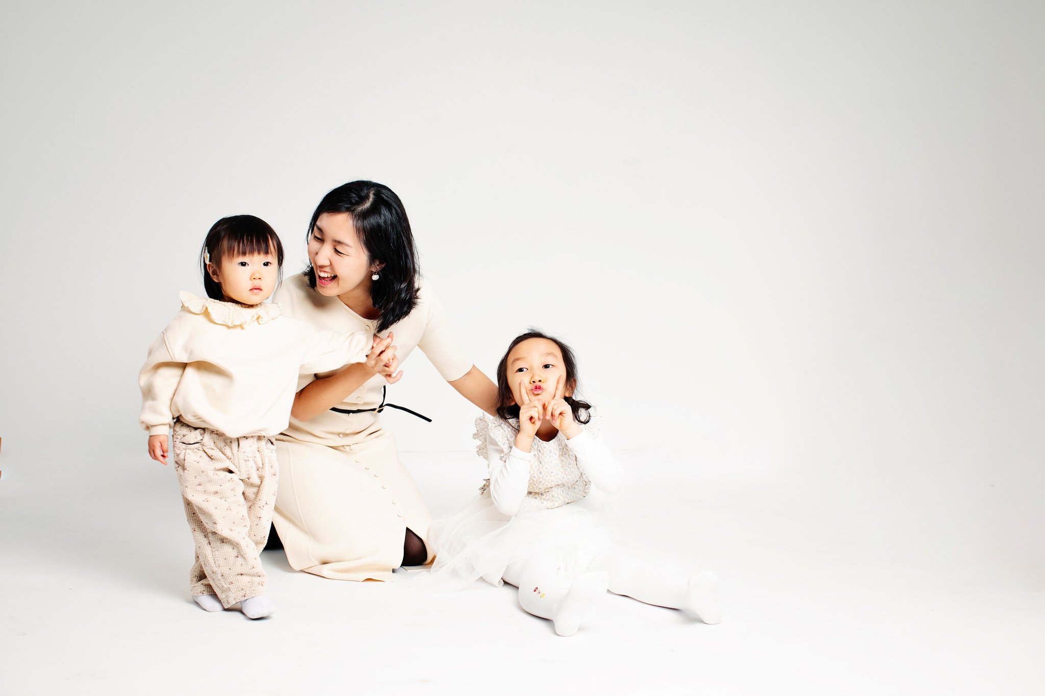 A mother on the floor with her two daughters, one making a silly face