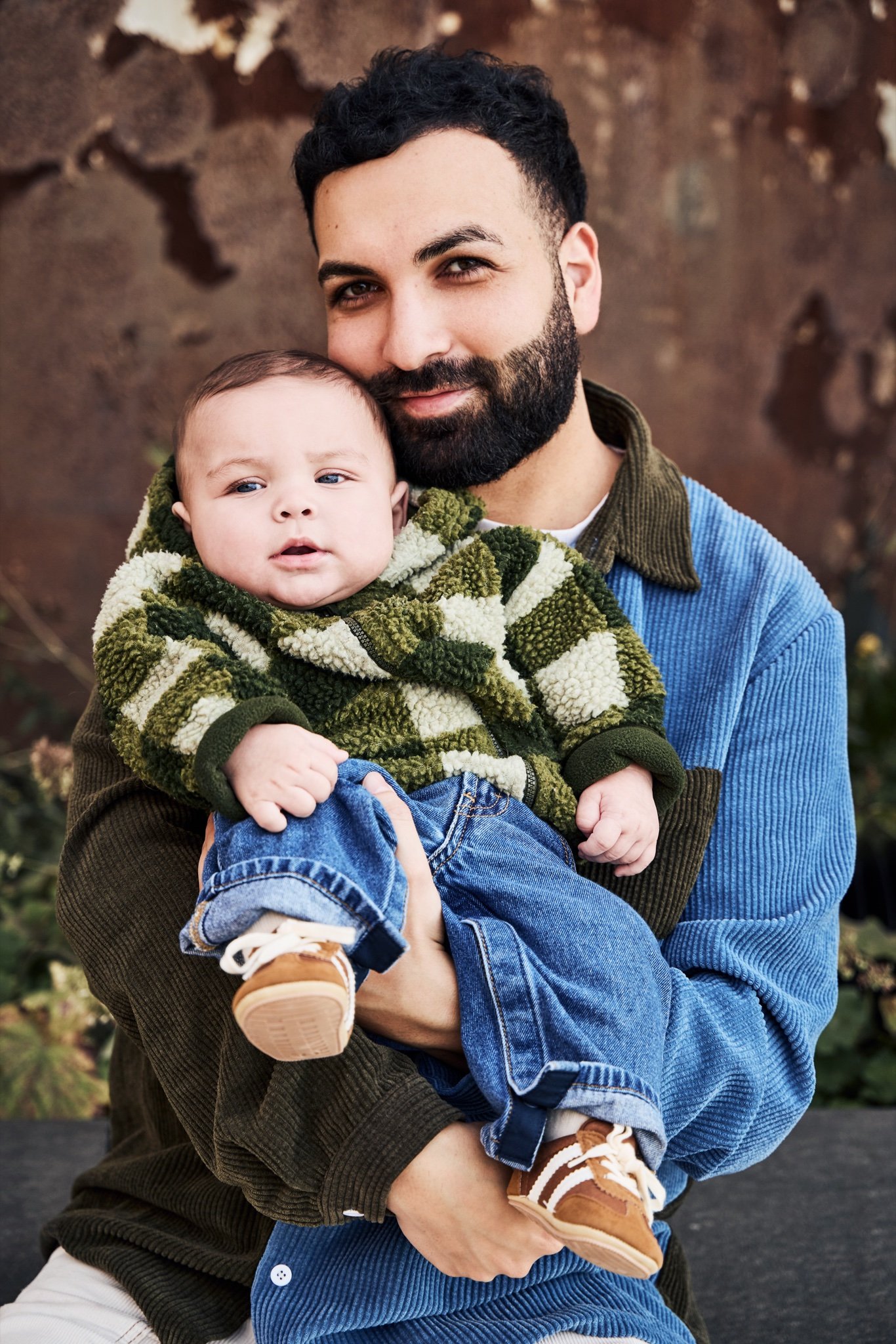 A father holding his baby son against a wall of rusted steel