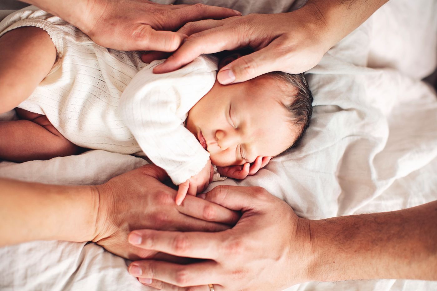 Parents' hands resting around a sleeping newborn