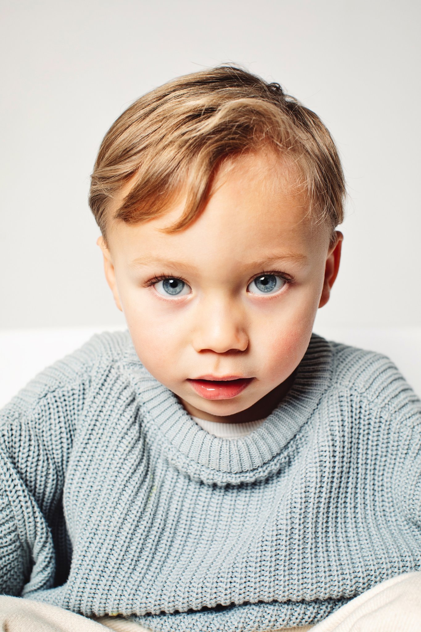 A boy sitting calmly on a white backdrop