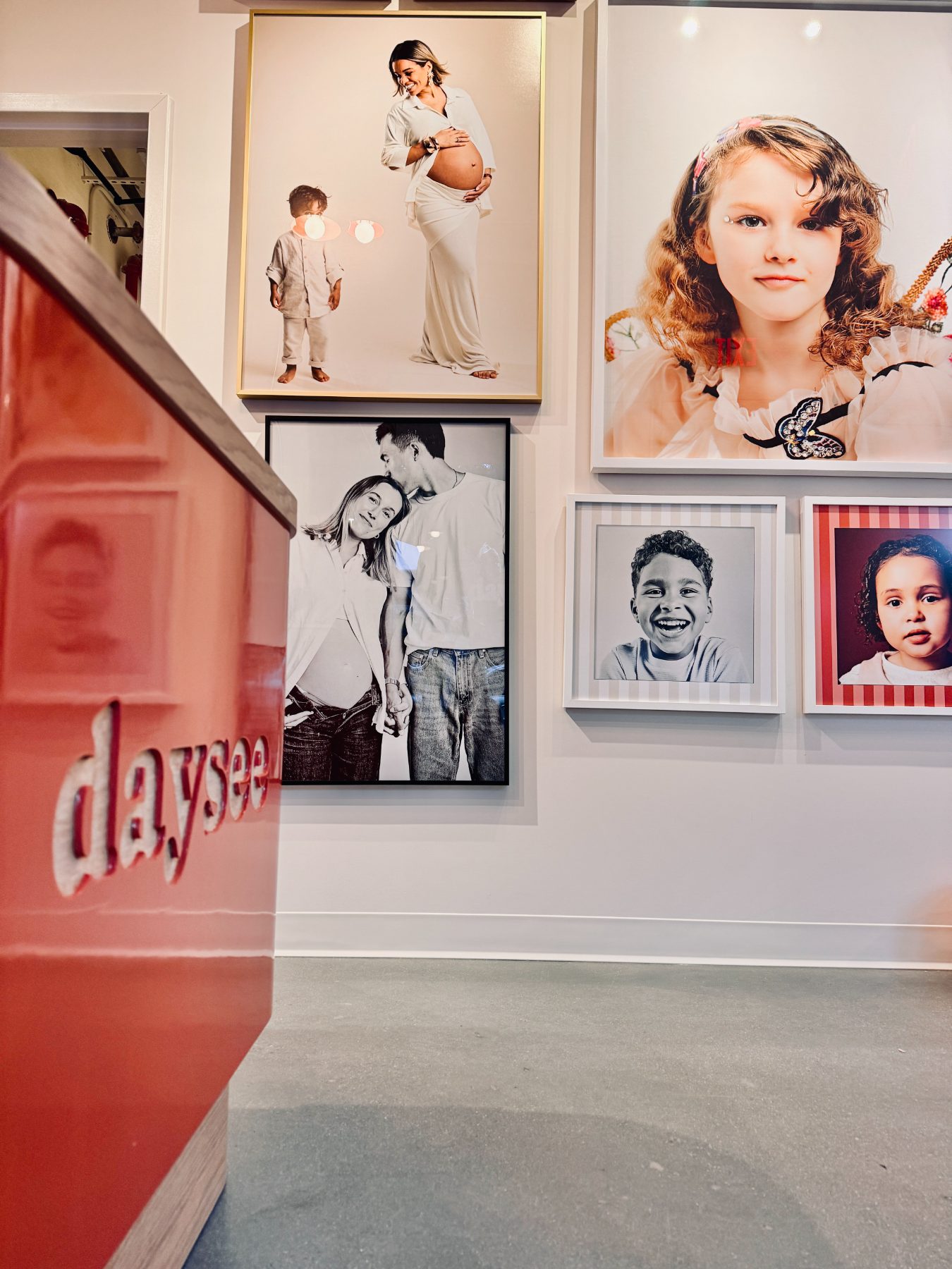 The portrait wall beside the red daysee reception desk, framed client portraits in mixed frames