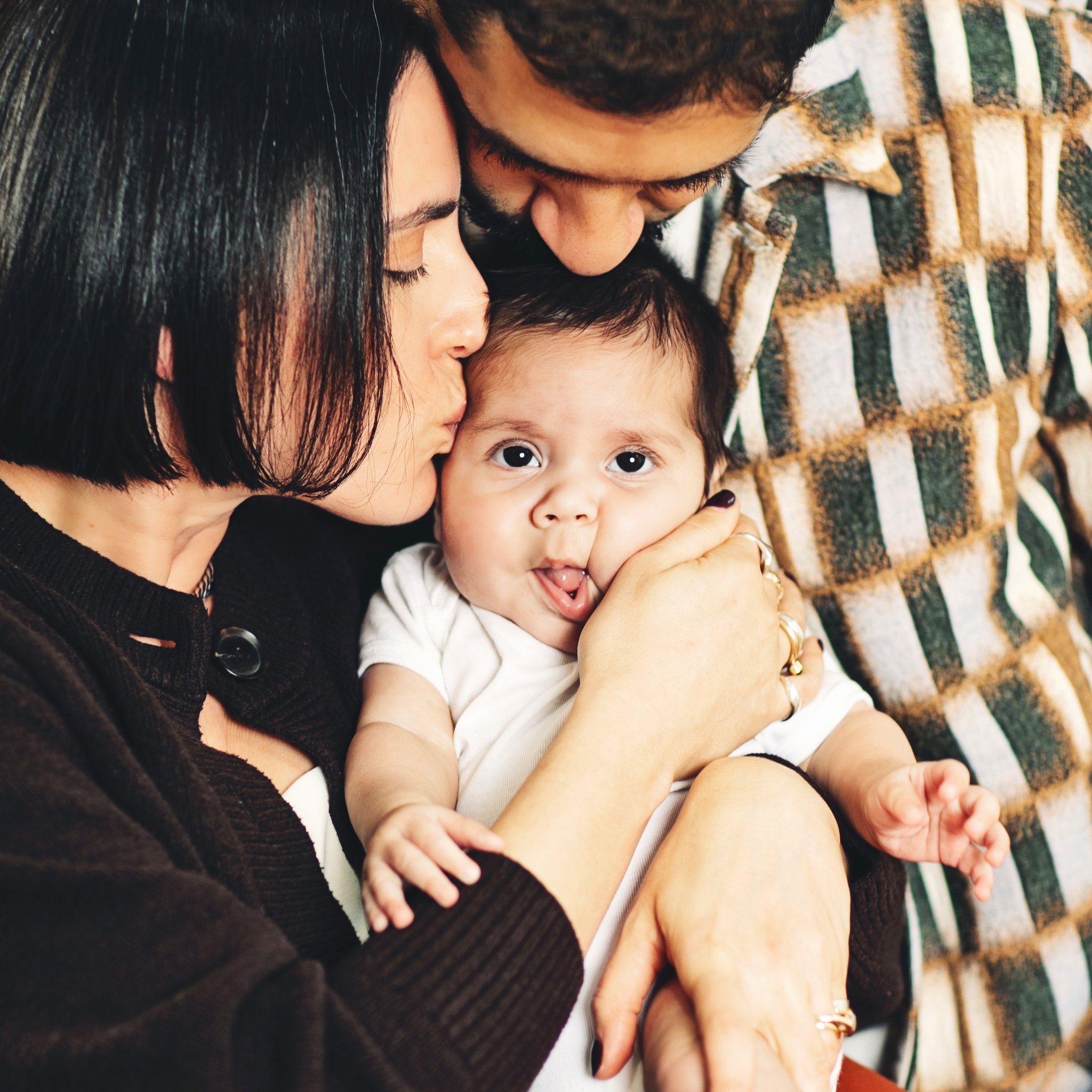Two parents kissing their newborn