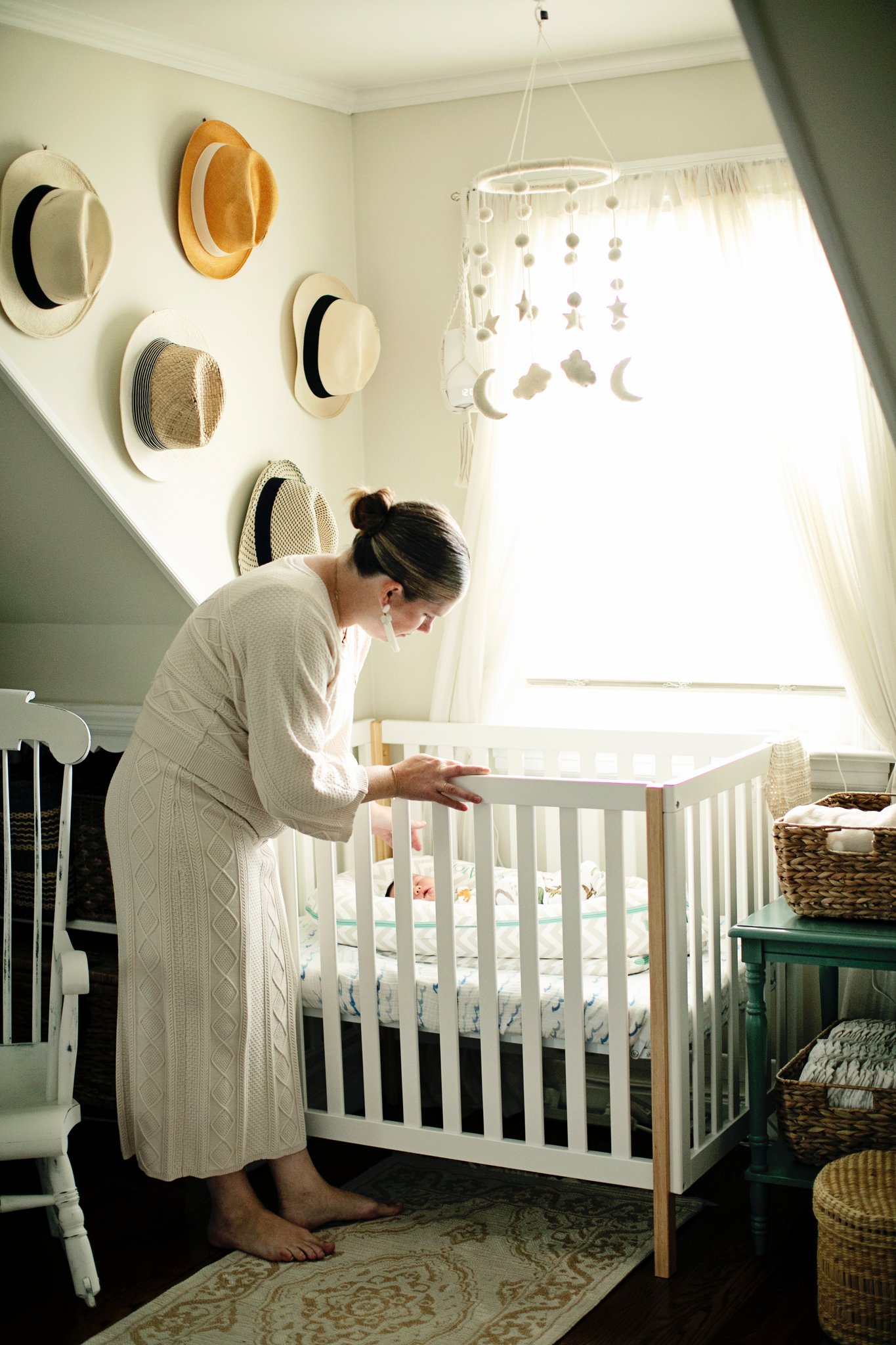 A mother leaning over the crib in a sunlit nursery