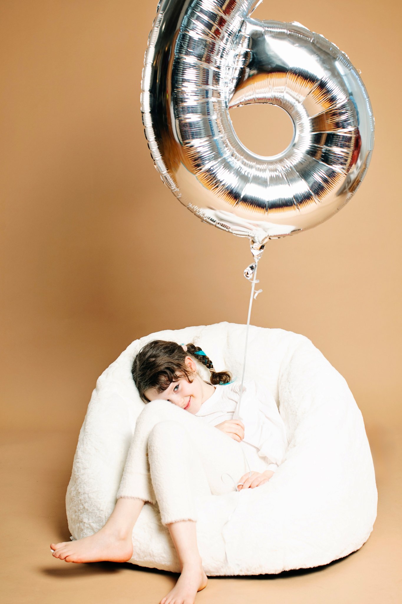 A girl on a beanbag with her birthday balloon on a tan backdrop