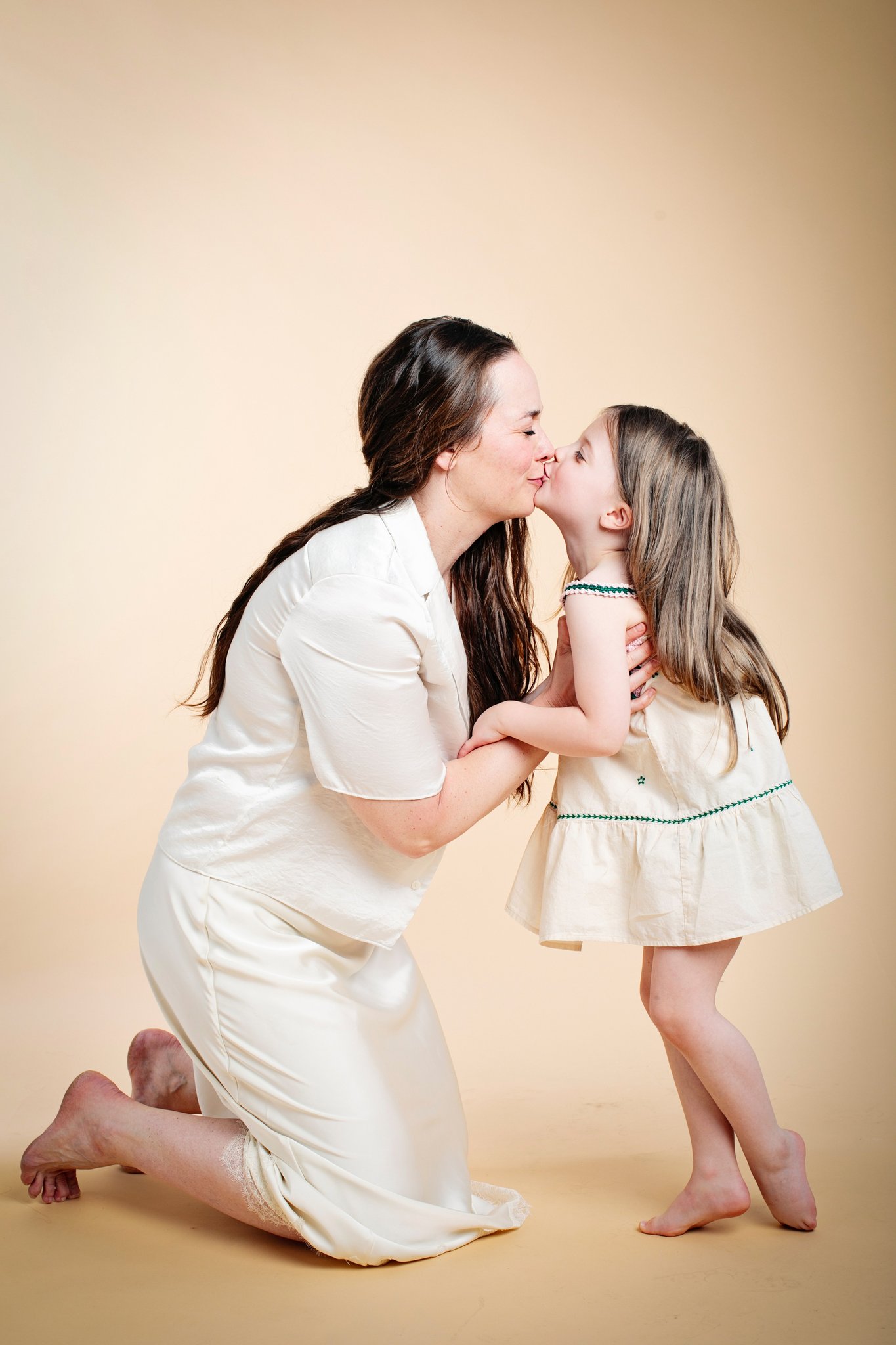 A mother kneeling to kiss her daughter