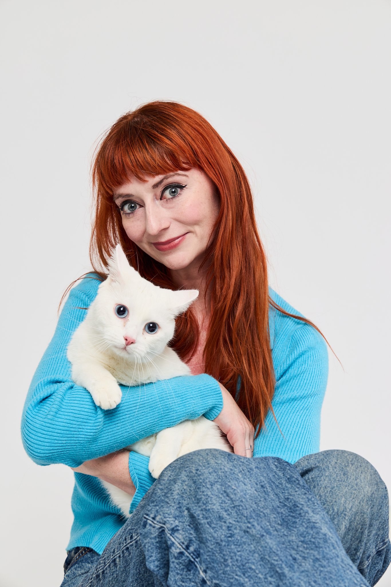 A red-haired woman in a blue jumper holding a white cat in her lap