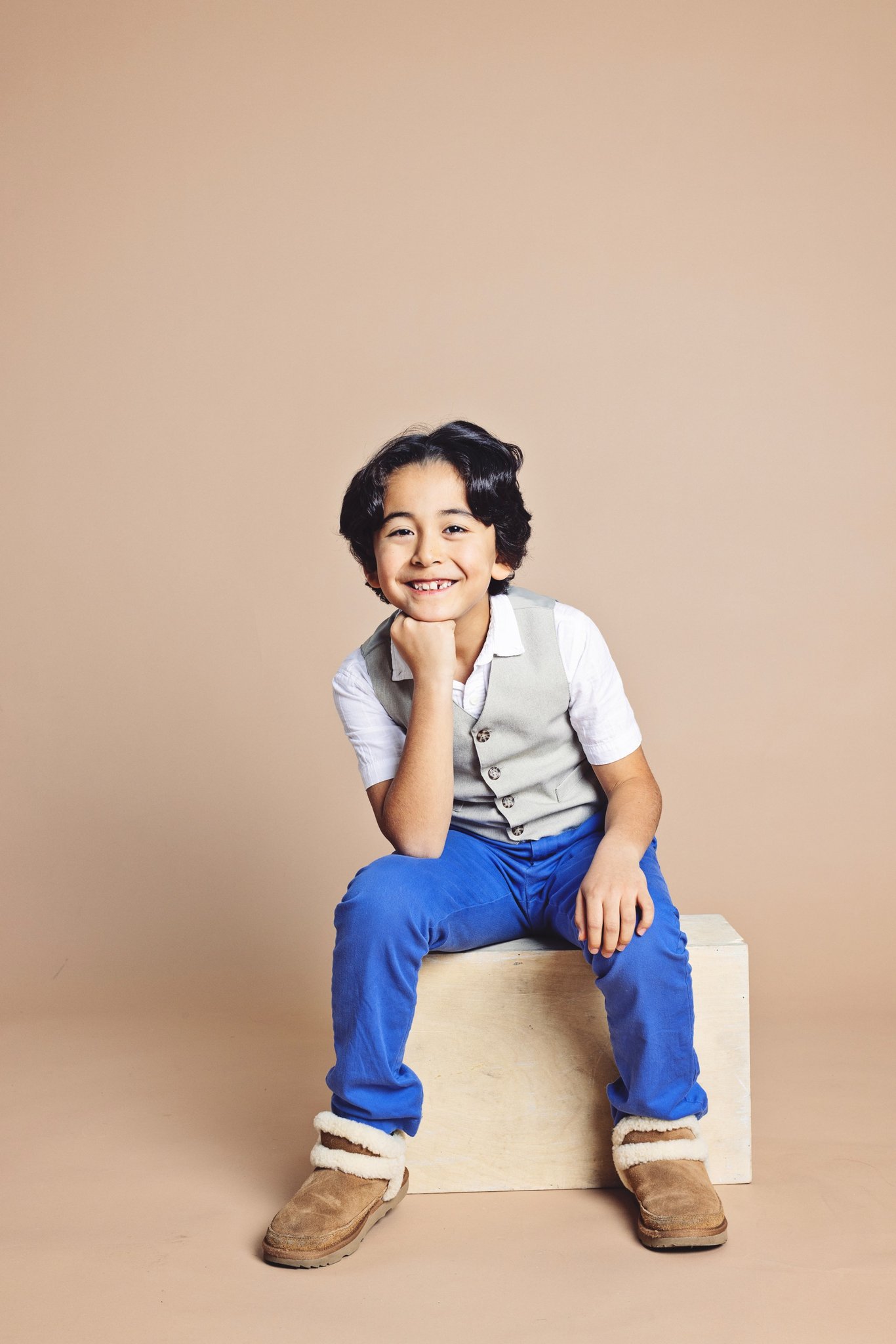 A boy in a grey vest sitting on a wooden crate