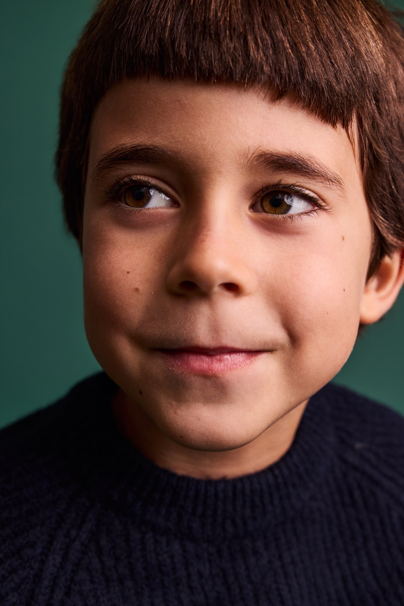 A close-up of a smiling boy with a fringe on the Evergreen backdrop