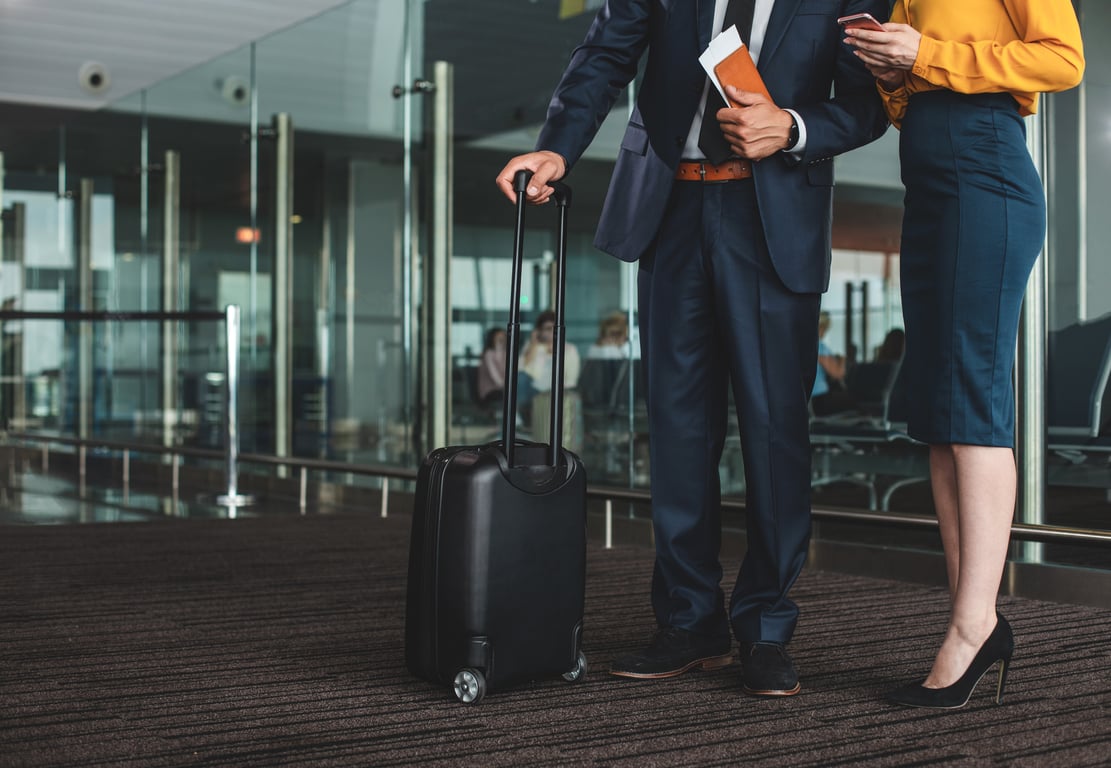 Business travelers with luggage waiting at an airport terminal.