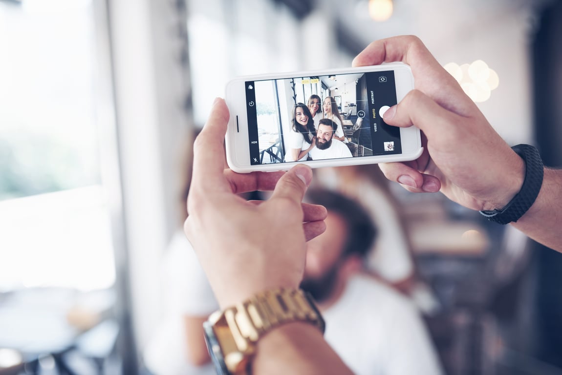 Close-up of hands holding a mobile phone, taking a video of friends at a cozy cafe.